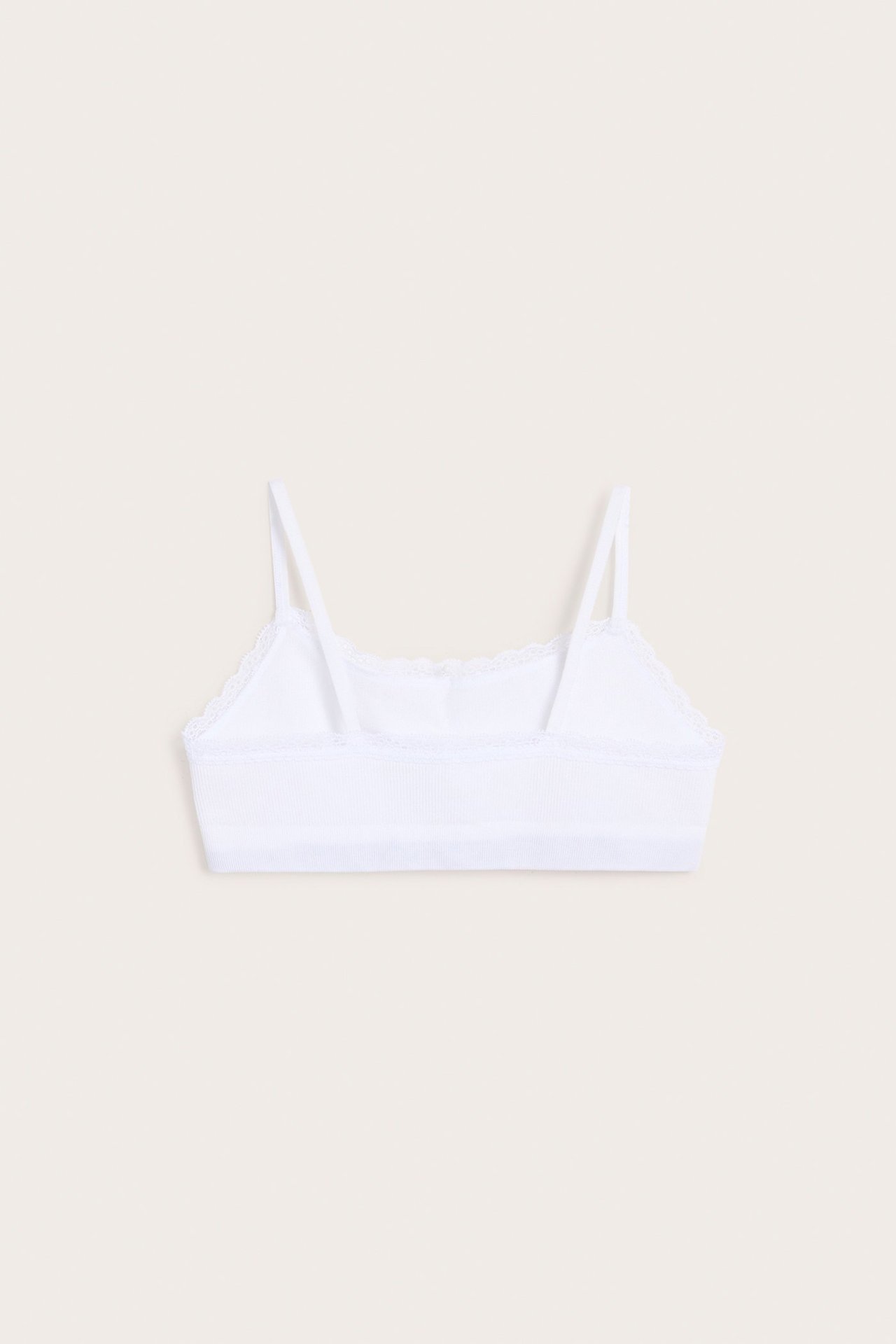 Widok z tyłu białego, bezszwowego, prążkowanego topu z cienkimi ramiączkami i koronką.