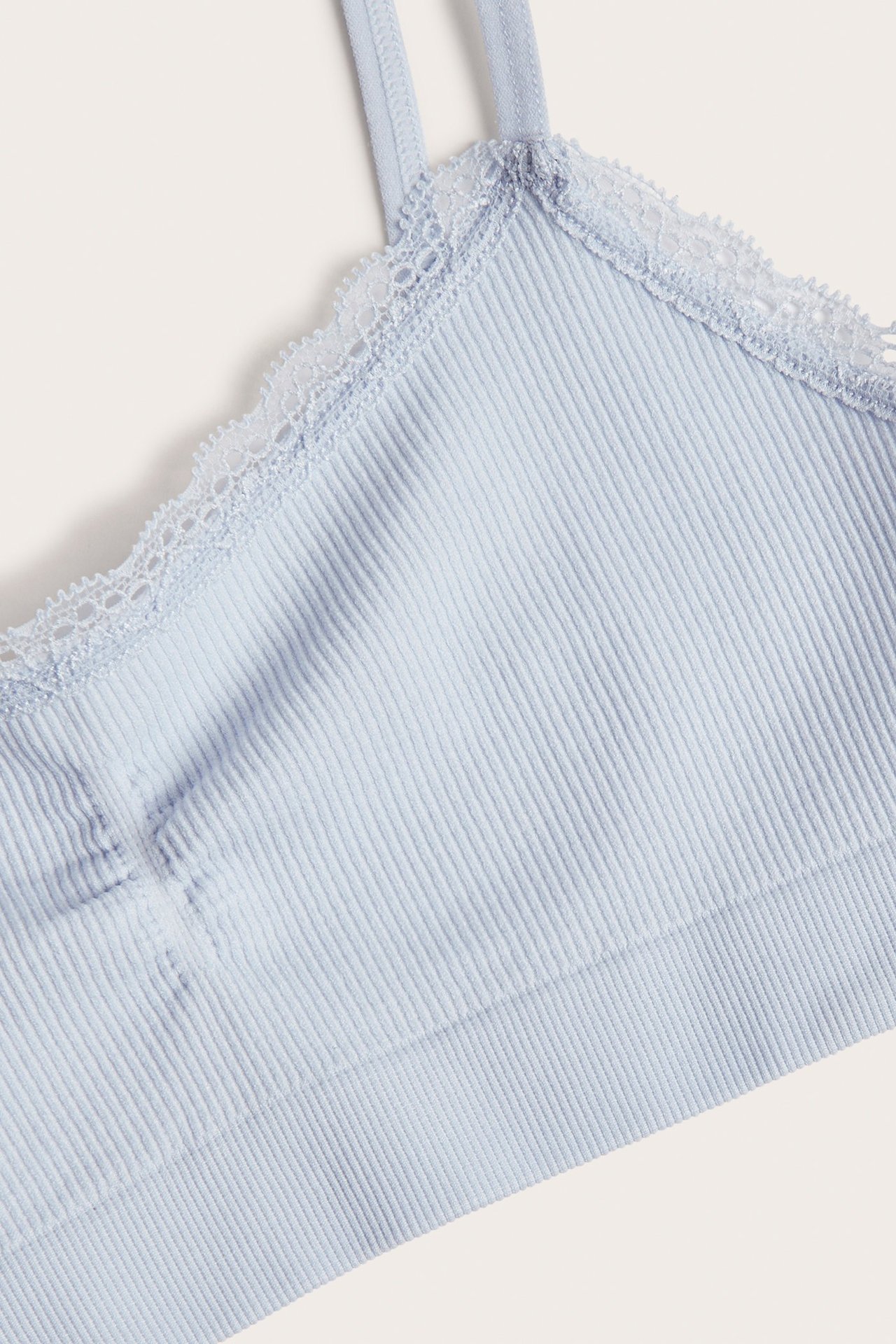 Nærbilde av en lyseblå sømløs ribbet topp med delikat blondekant langs halslinningen.