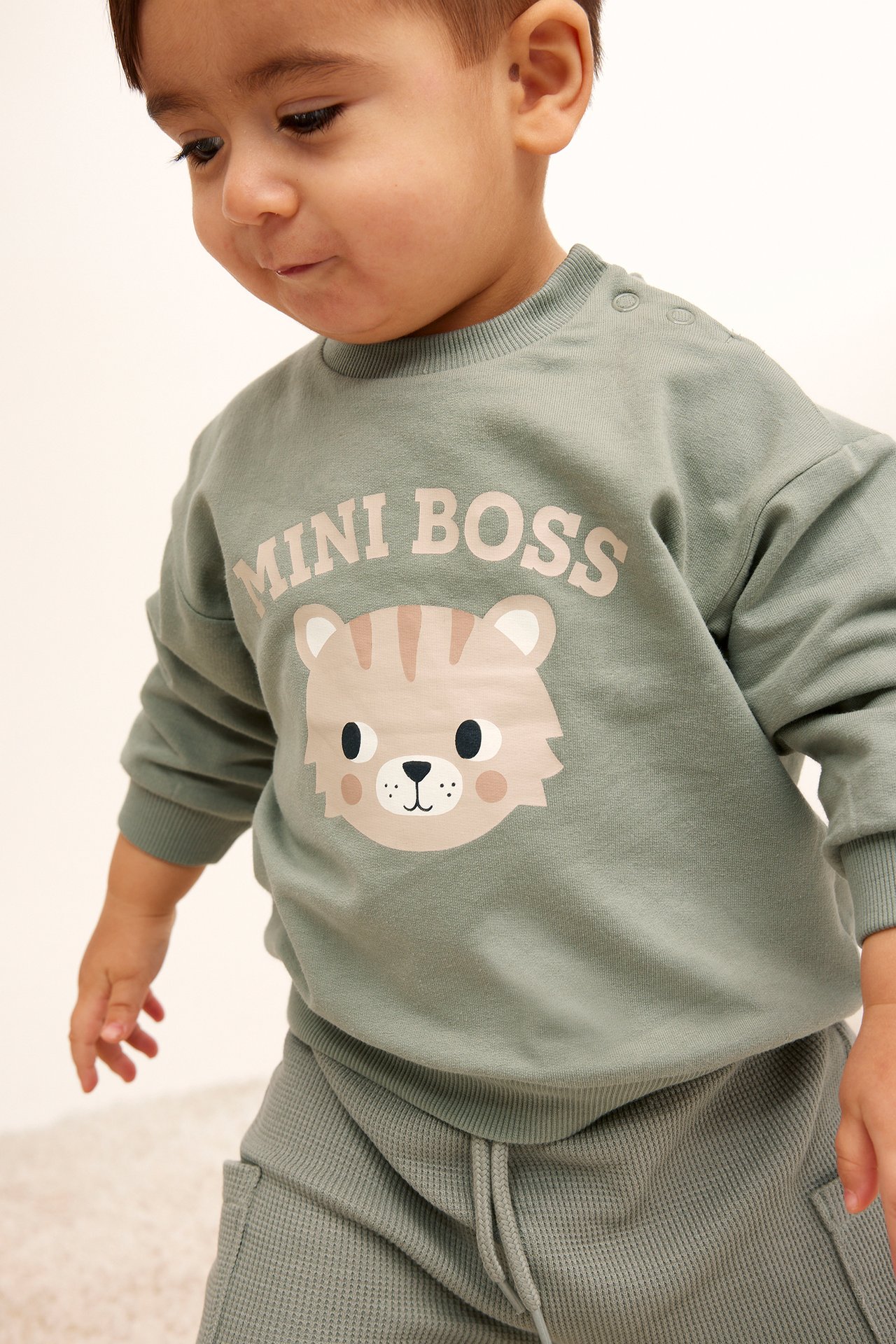 Edestä näkymä vauvasta vihreässä puuvillapaidassa, jossa 'MINI BOSS' tiikeriprintti ja yhteensopivat vohvelihousut.