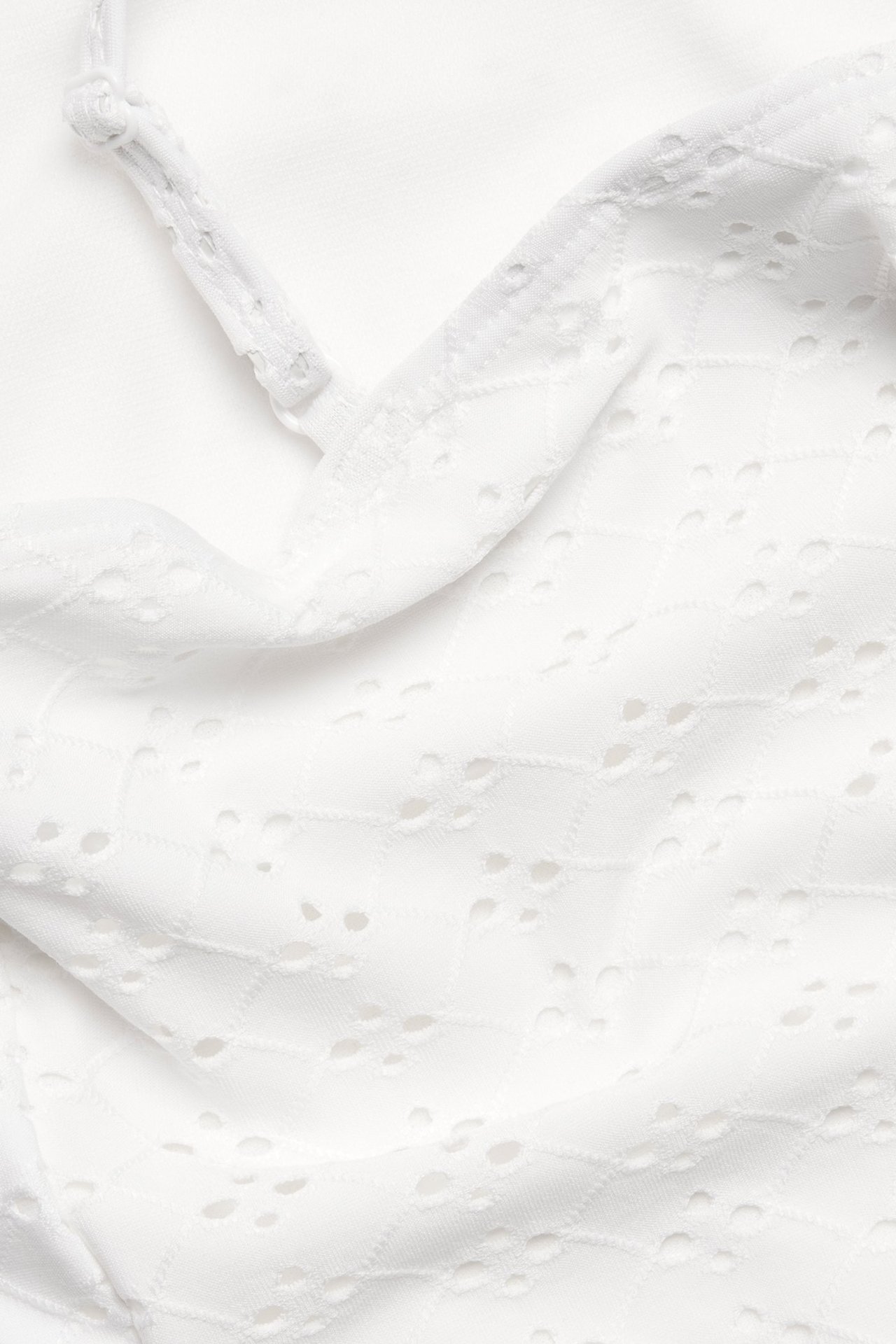 Lähikuva luonnonvalkoisesta uimapuvusta, jossa broderie anglaise -kuvio ja ohuet olkaimet.