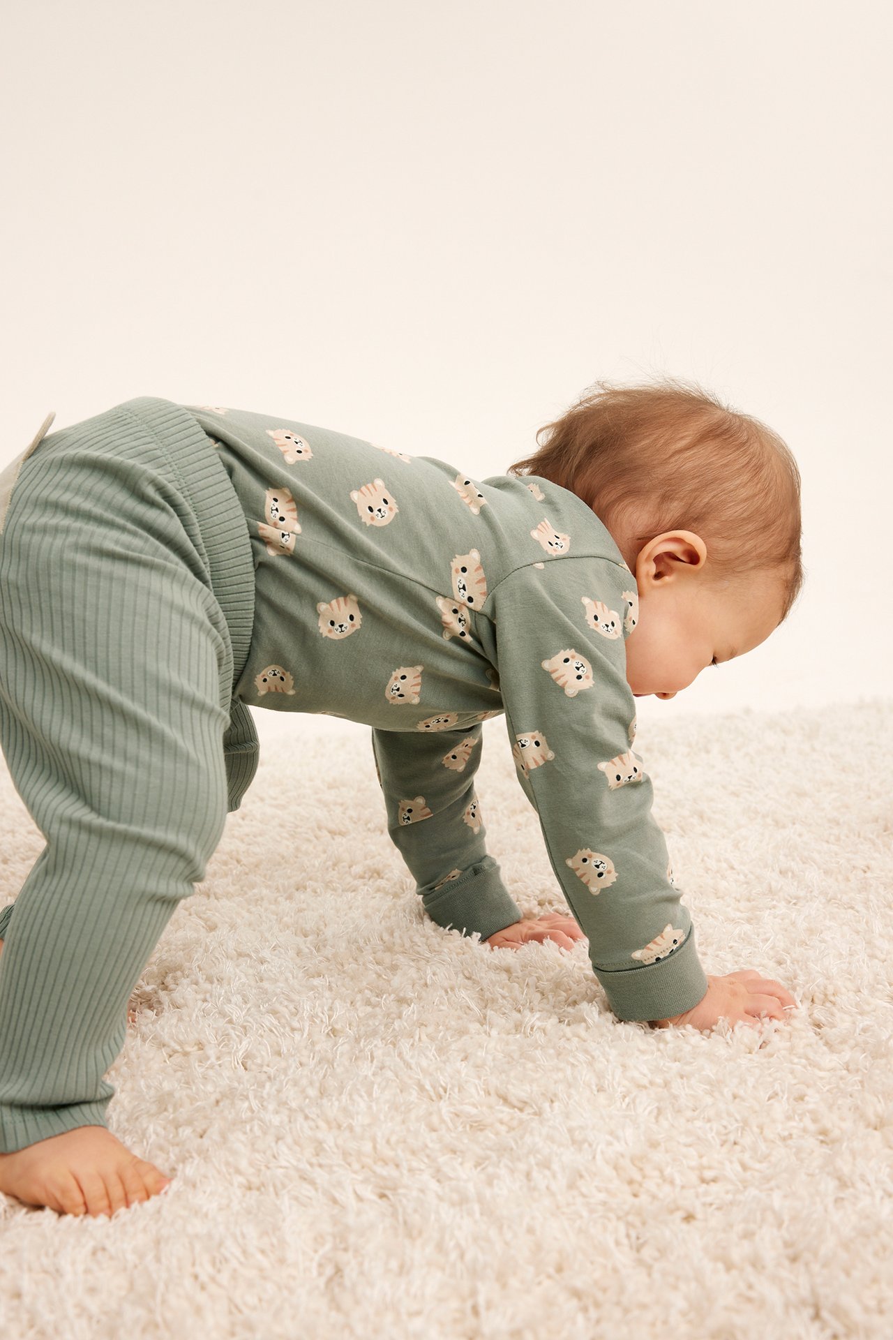 Krypande baby i mörkgrön kattmönstrad långärmad body och salviagröna ribbade leggings.