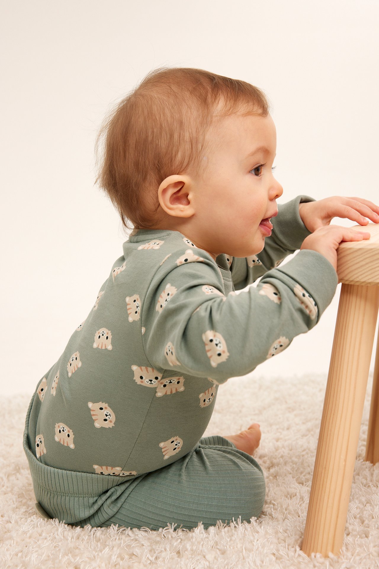 Sidovy av en baby i en mörkgrön långärmad body med kattmönster och matchande ribbade leggings.