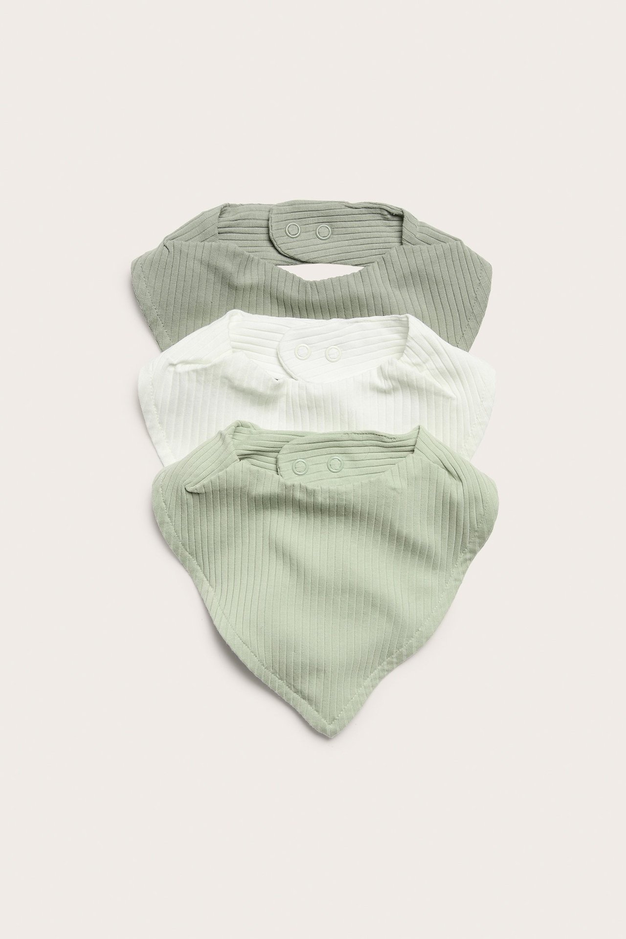 Framifrån: tre ribbade babyhaklappar, två gröna och en vit, med tryckknappar bak.
