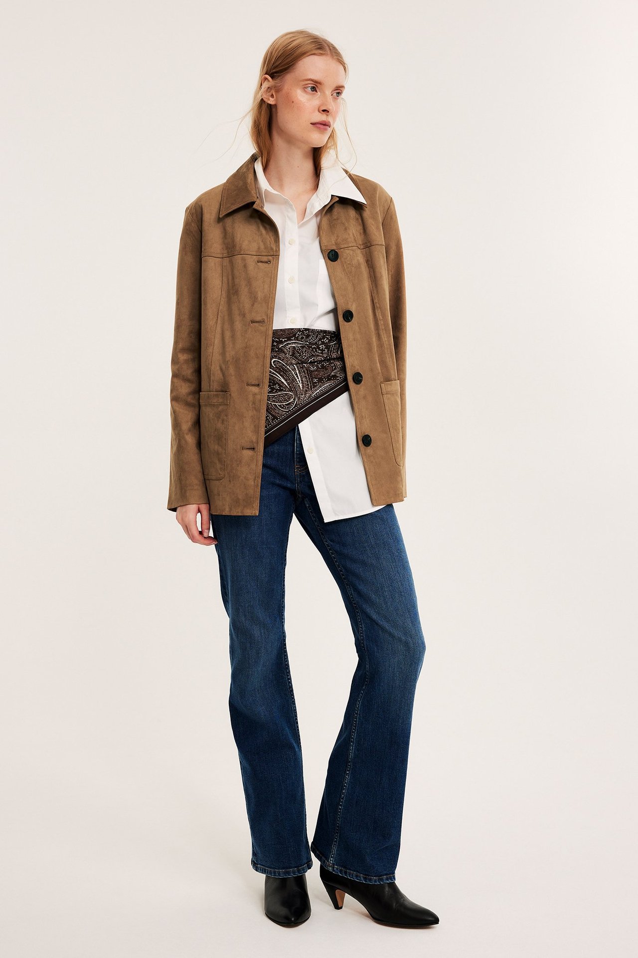 Edestä: Nainen ruskeassa mokkajäljitelmätakissa, valkoisessa paidassa, sinisissä farkuissa, mustissa saappaissa.