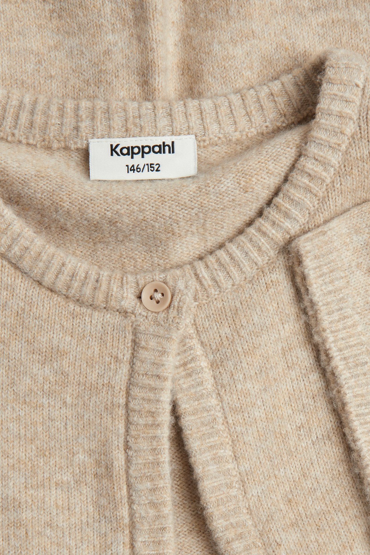 Nærbilde av en kortermet strikket cardigan for barn i beige melange med én knapp i halsen.