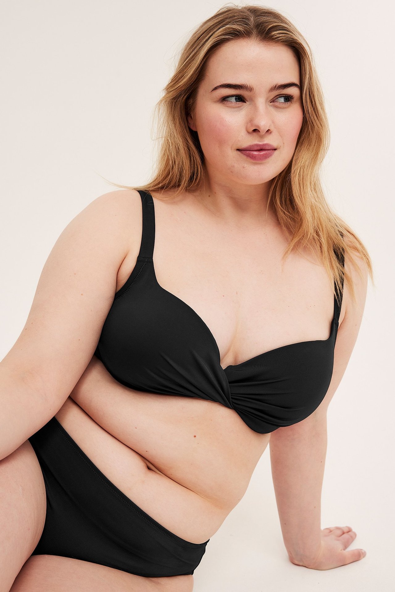 Widok z przodu kobiety w czarnym biustonoszu bikini z fiszbinami, skręconym przodem i pasującymi figami.