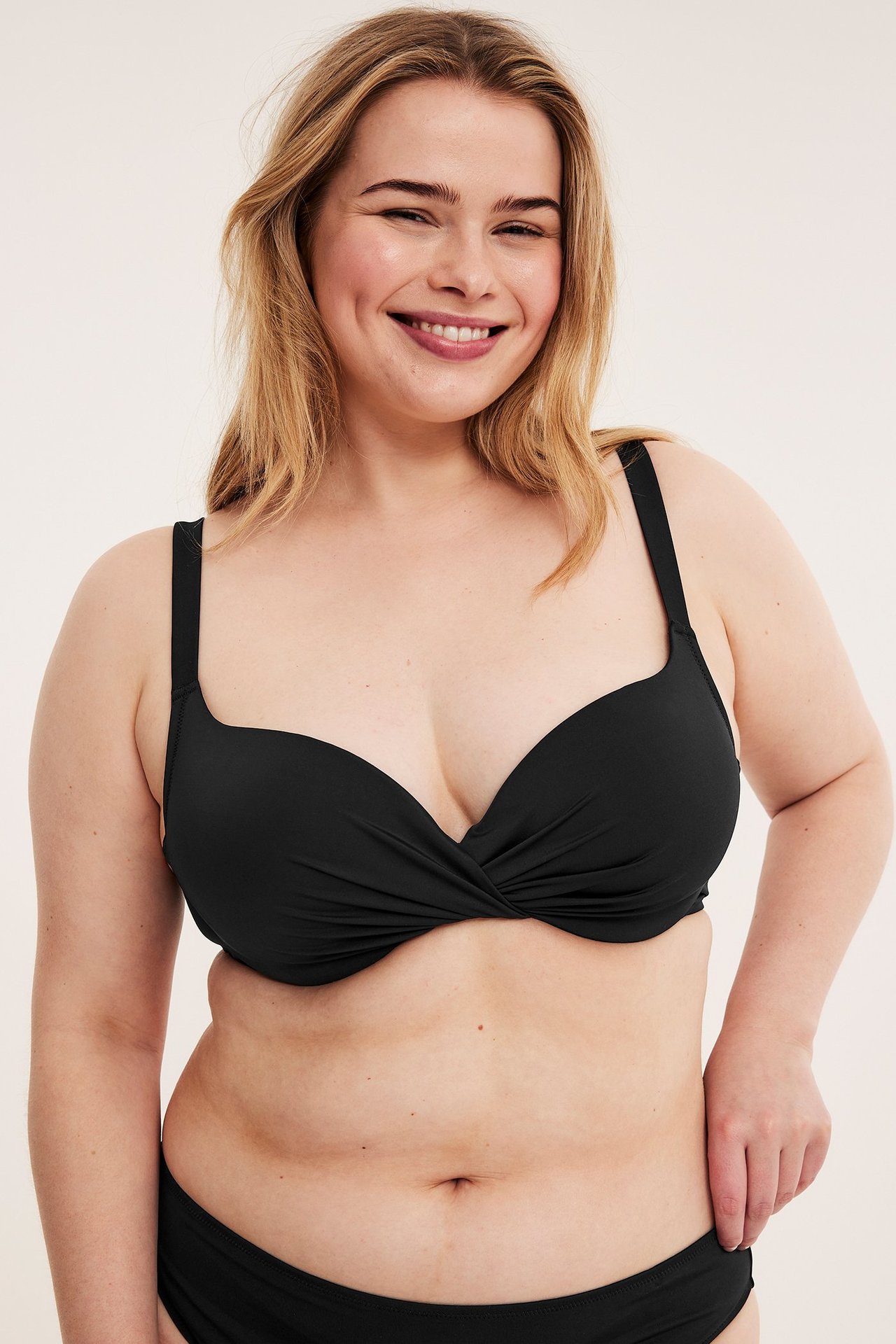 Widok z przodu uśmiechniętej kobiety w czarnym, jednolitym biustonoszu bikini ze skręconym przodem i pasującymi figami.