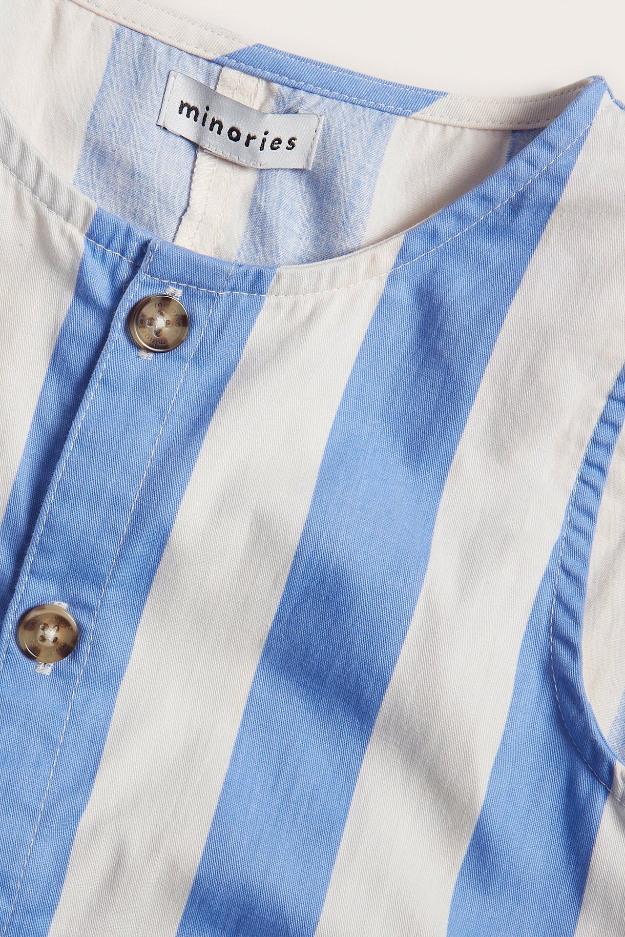 Zbliżenie z przodu na dziecięcy kombinezon z bawełny w niebiesko-białe pasy z brązowymi guzikami.