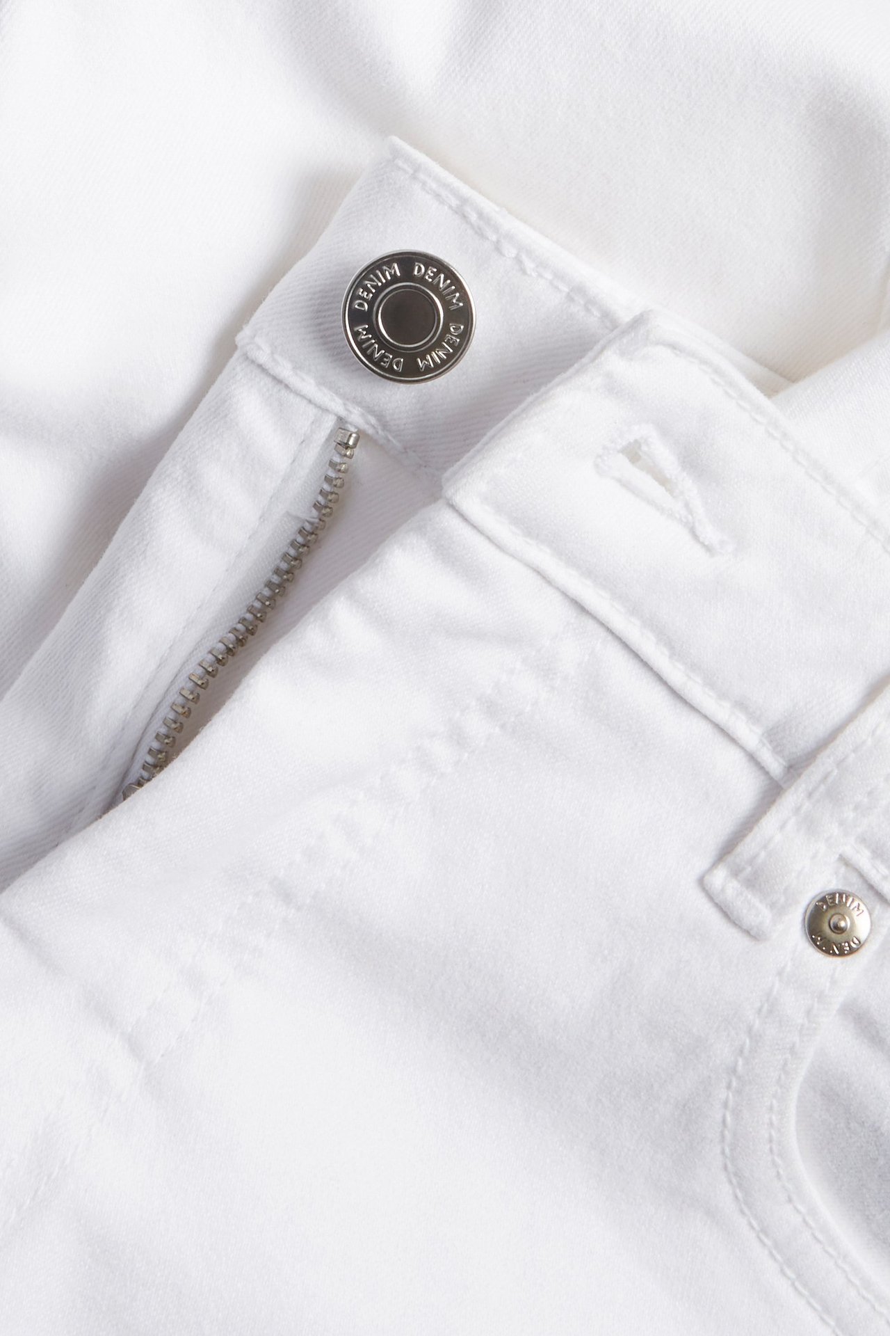 Zbliżenie na białe dżinsy cropped z wysokim stanem, ze srebrnym guzikiem i zamkiem błyskawicznym.