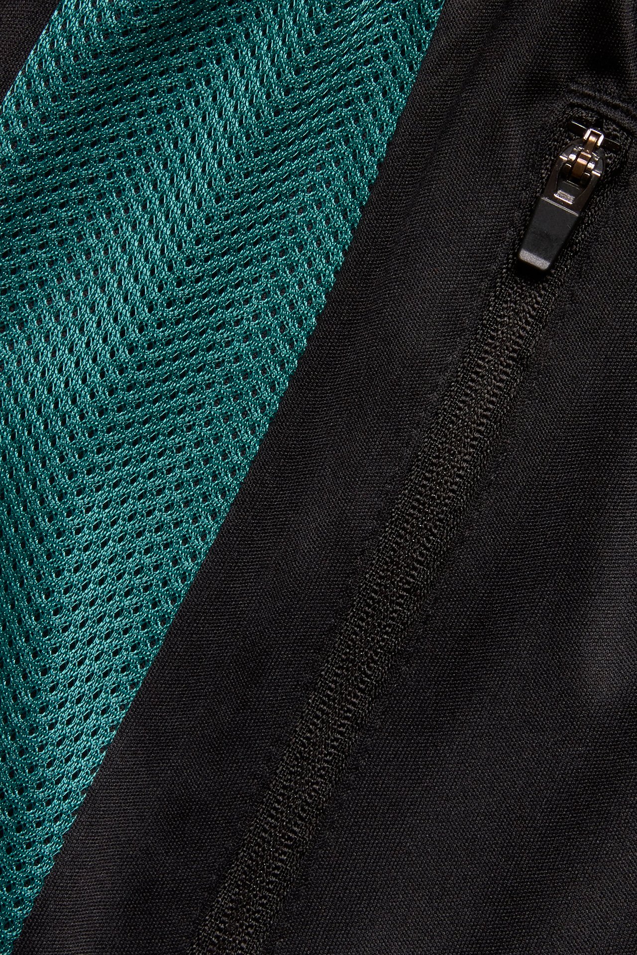 Närbild av svarta träningsshorts med en turkos chevronmönstrad meshpanel och svart dragkedja.