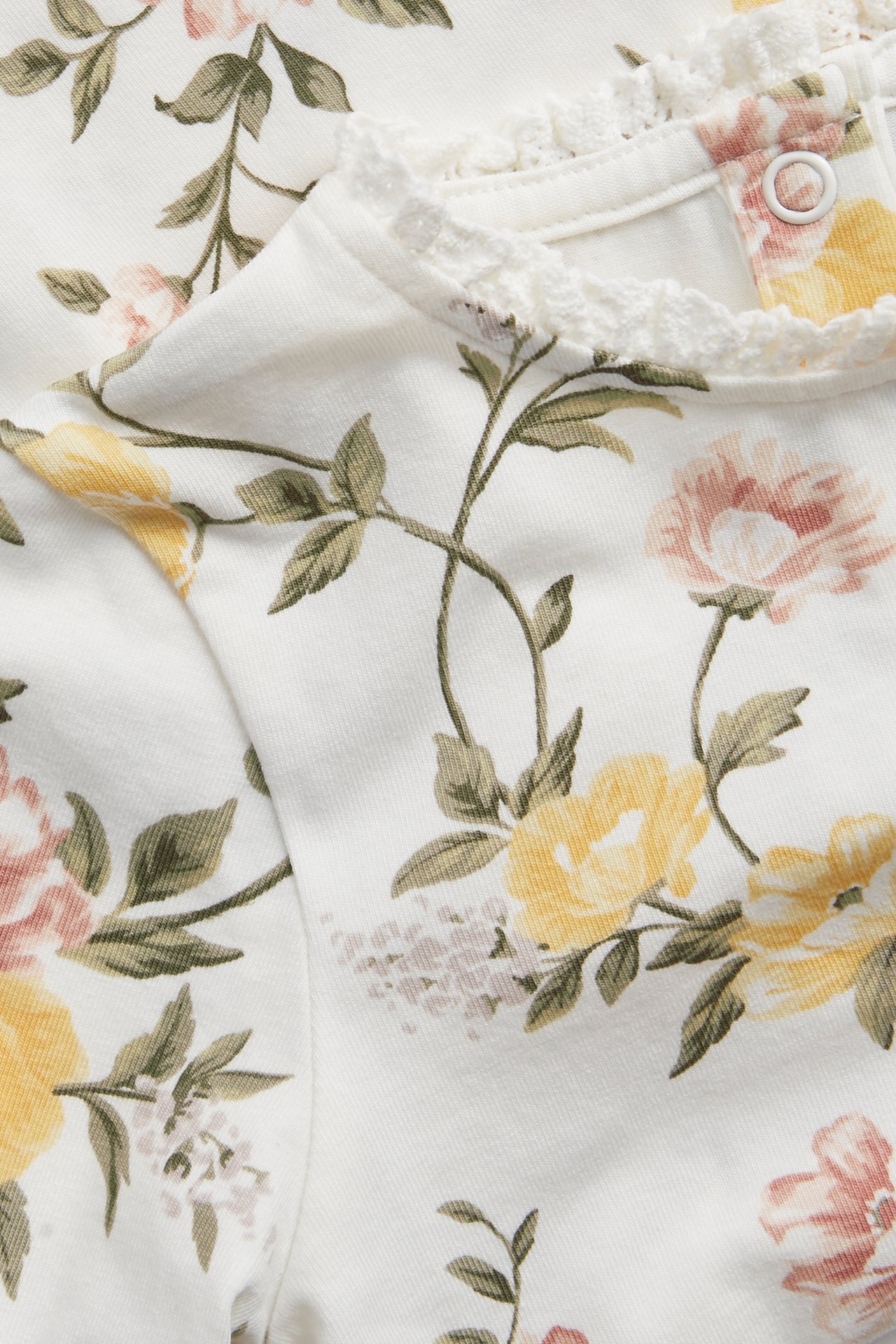 Nærbilde av en offwhite baby-/barns blomstret jerseytop med gule/rosa roser og blondekant i halsen.