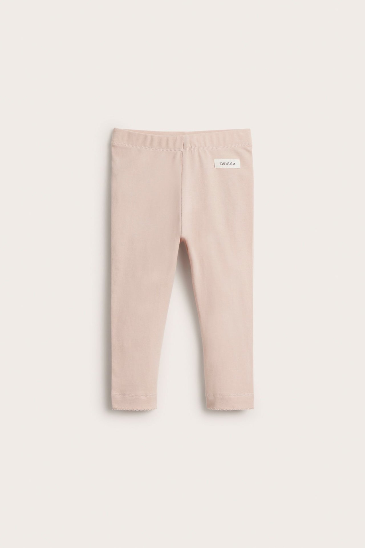 Frontvy av ljusrosa baby-leggings med resår i midjan och vågig spetskant vid bensluten.