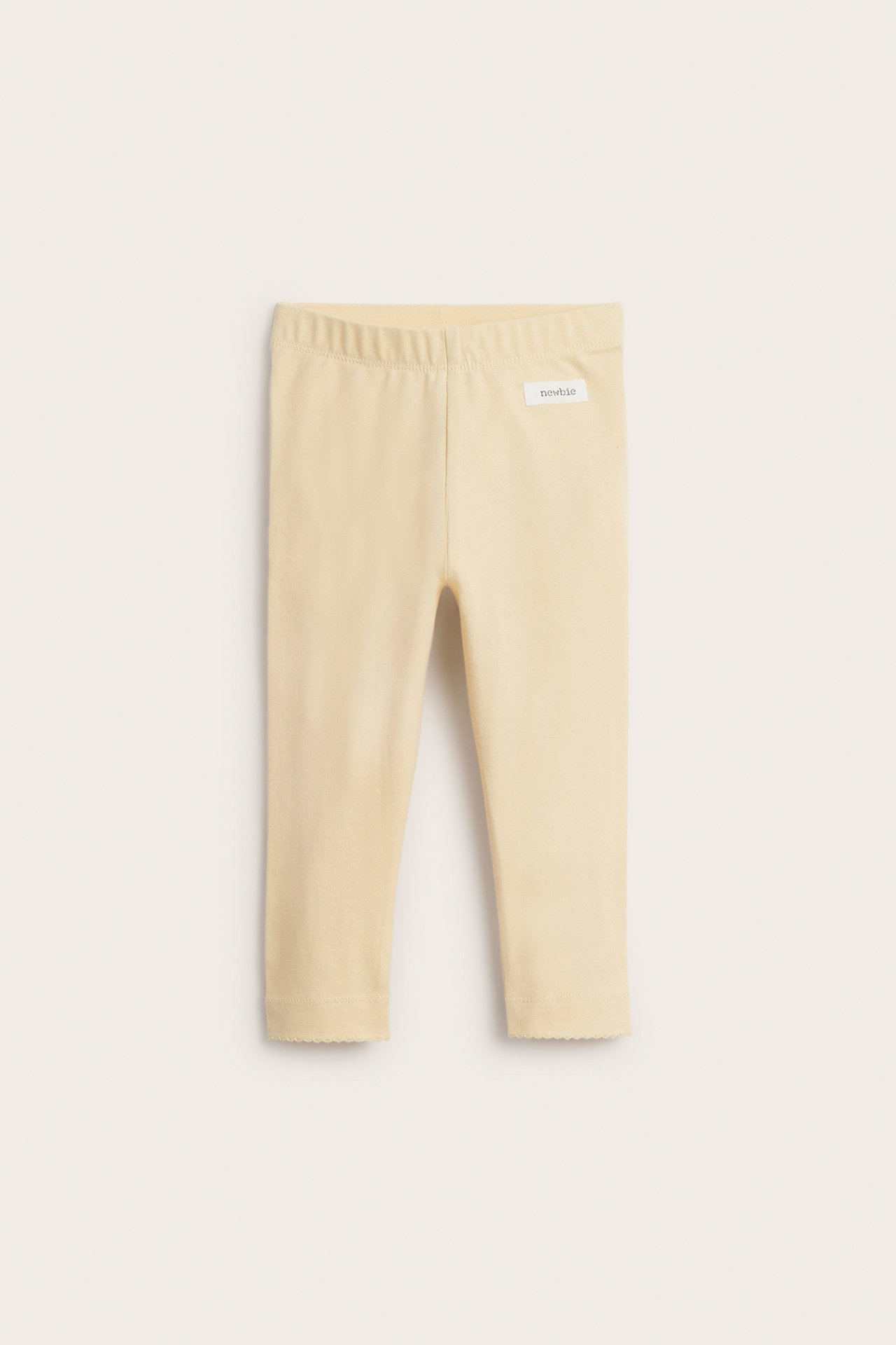 Framifrån, ljusgula baby-leggings med resår i midjan och vågiga benslut.