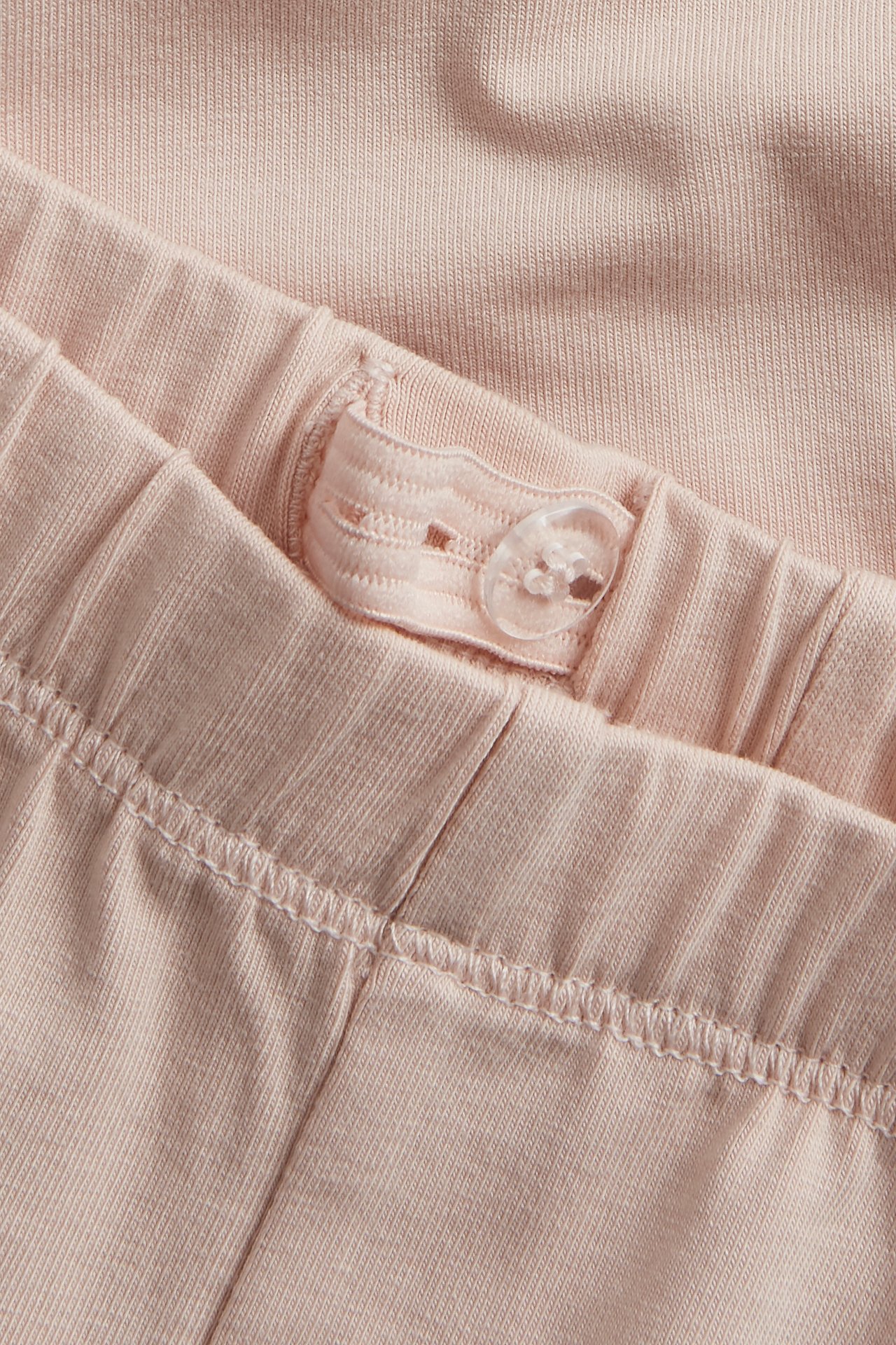 Nærbilde av lyserosa leggings med justerbar elastisk linning og en gjennomsiktig knapp.