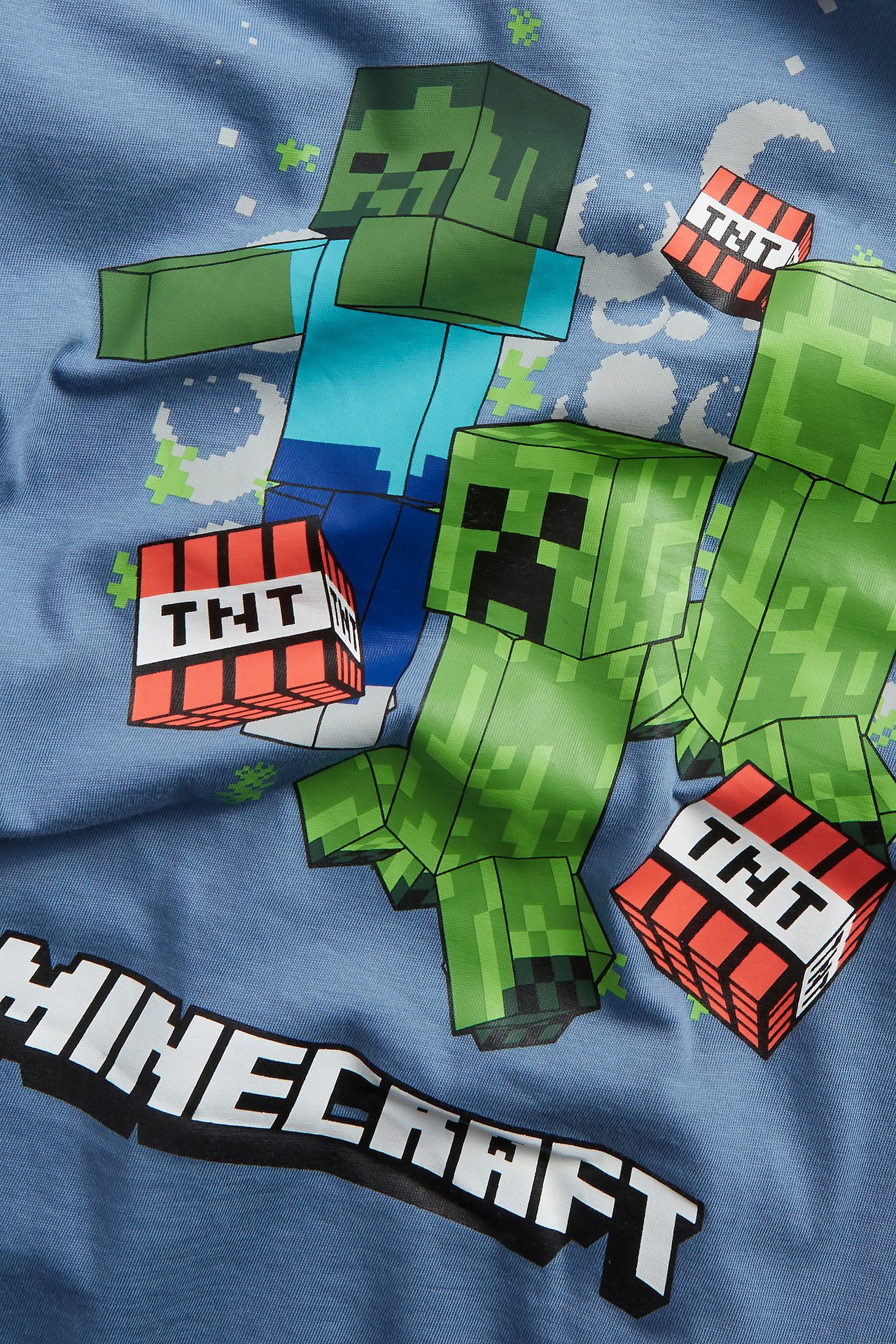 Zbliżenie na niebieską bawełnianą koszulkę dziecięcą z kolorowym nadrukiem postaci i logo Minecraft.