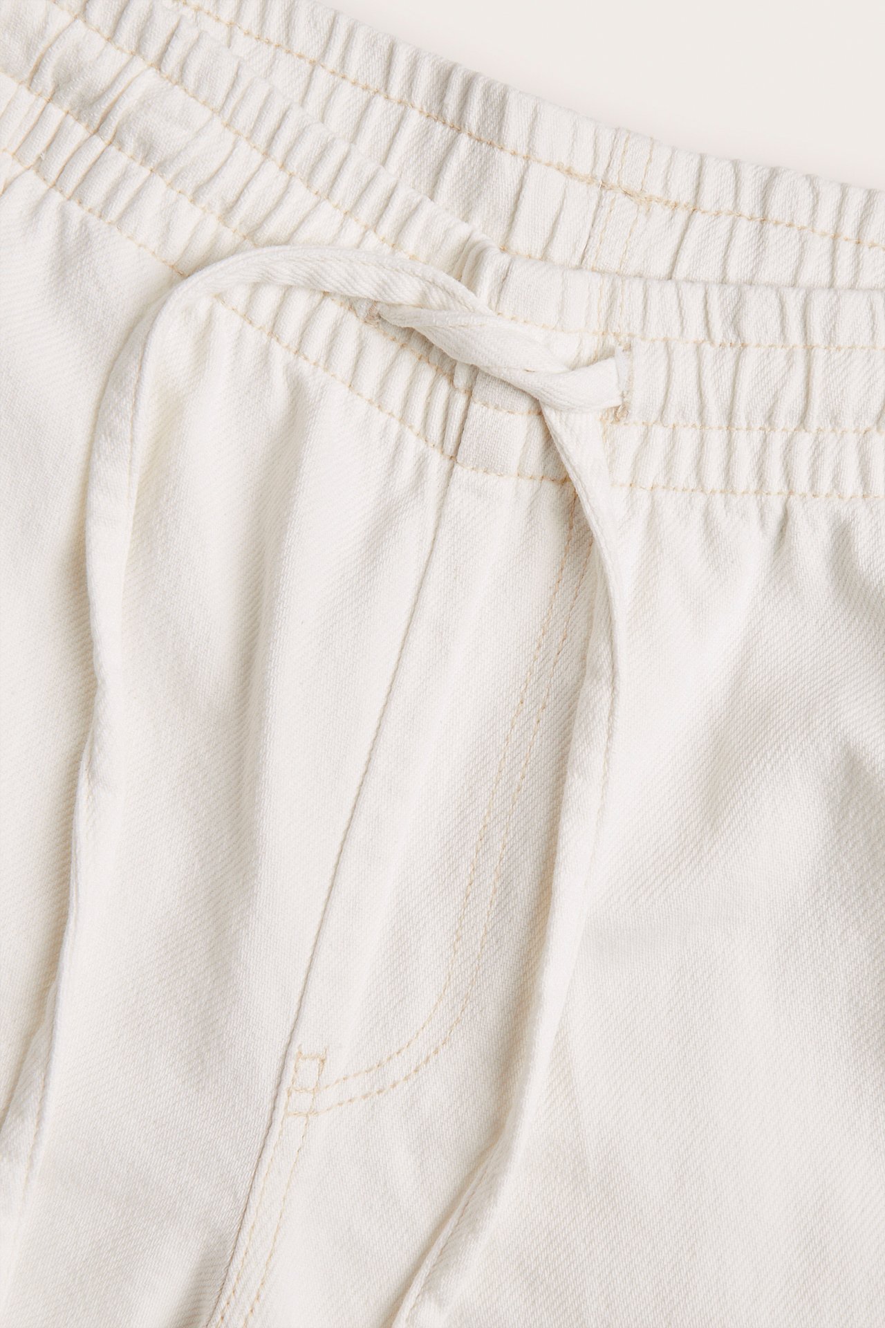 Nærbilde av hvite vide pull-on jeans i bomull med elastisk høy midje og snøring.