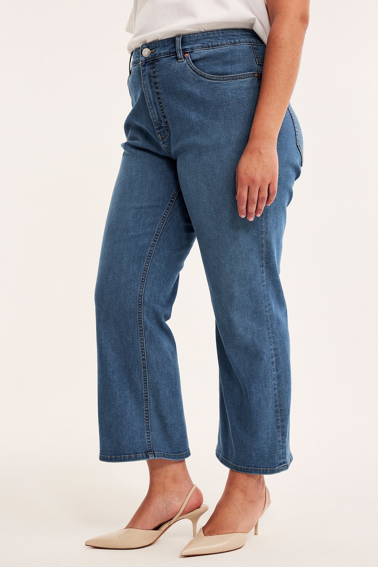 Sidovy av kvinna i blå denim high waist cropped flare jeans, vit t-shirt och beiga klackskor.