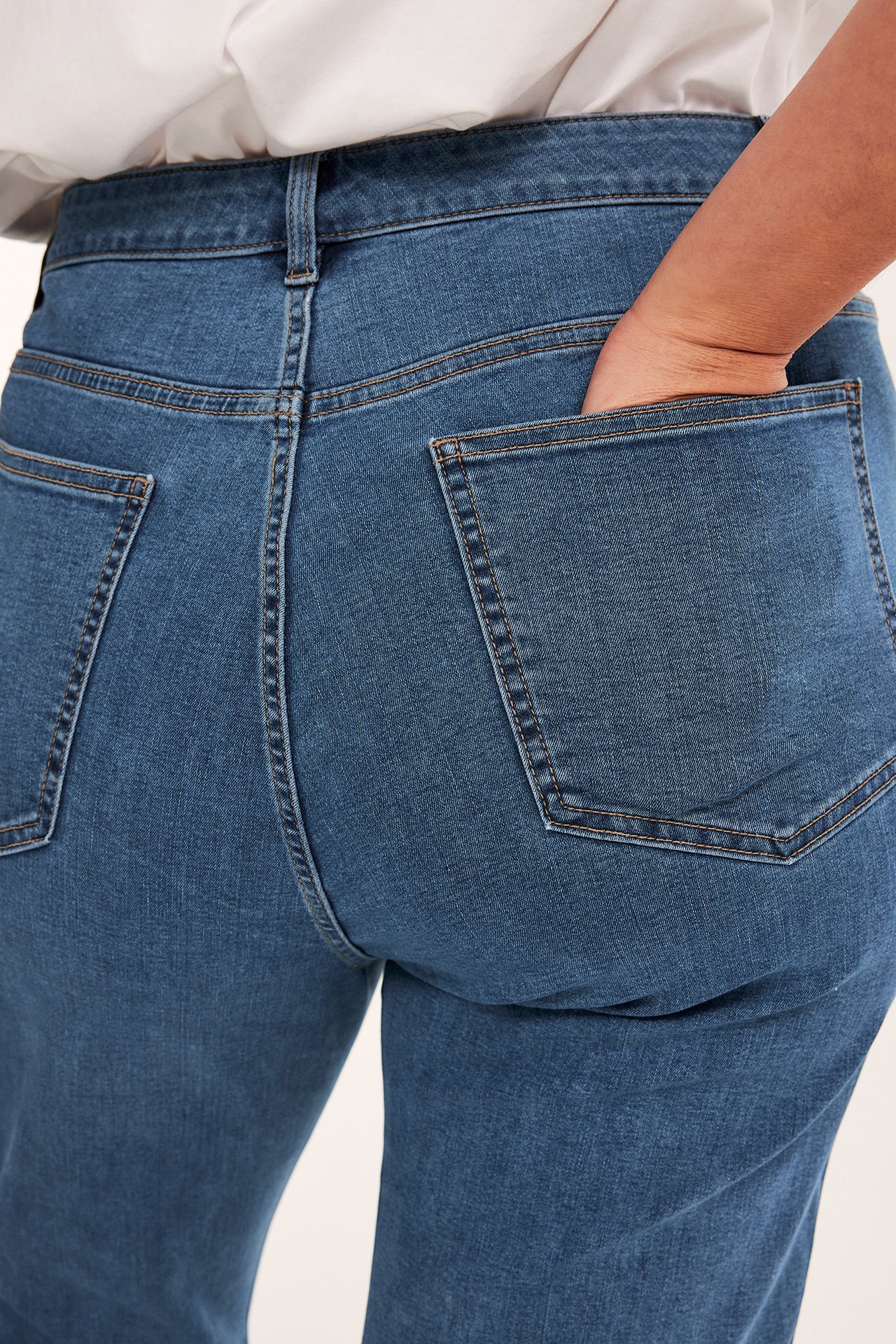Bakfra, kvinne i blå høye cropped flare jeans med hånden i høyre baklomme.