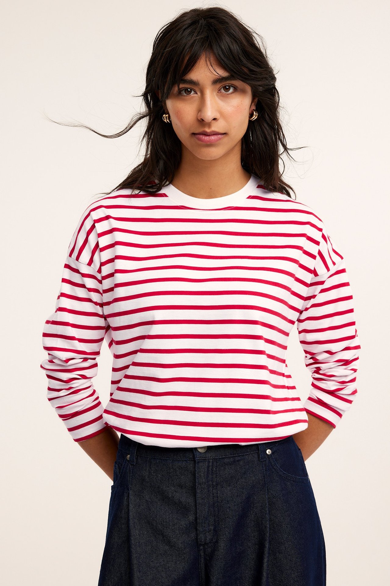 Widok z przodu kobiety w czerwono-białej bluzce w paski z długim rękawem i ciemnoniebieskich dżinsach.
