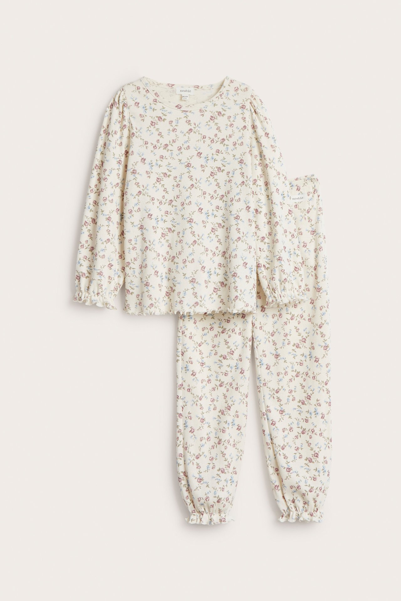 Edestä näkymä: luonnonvalkoinen ribattu 2-osainen puuvillapyjama, jossa kukkakuvio ja röyhelöreunat.