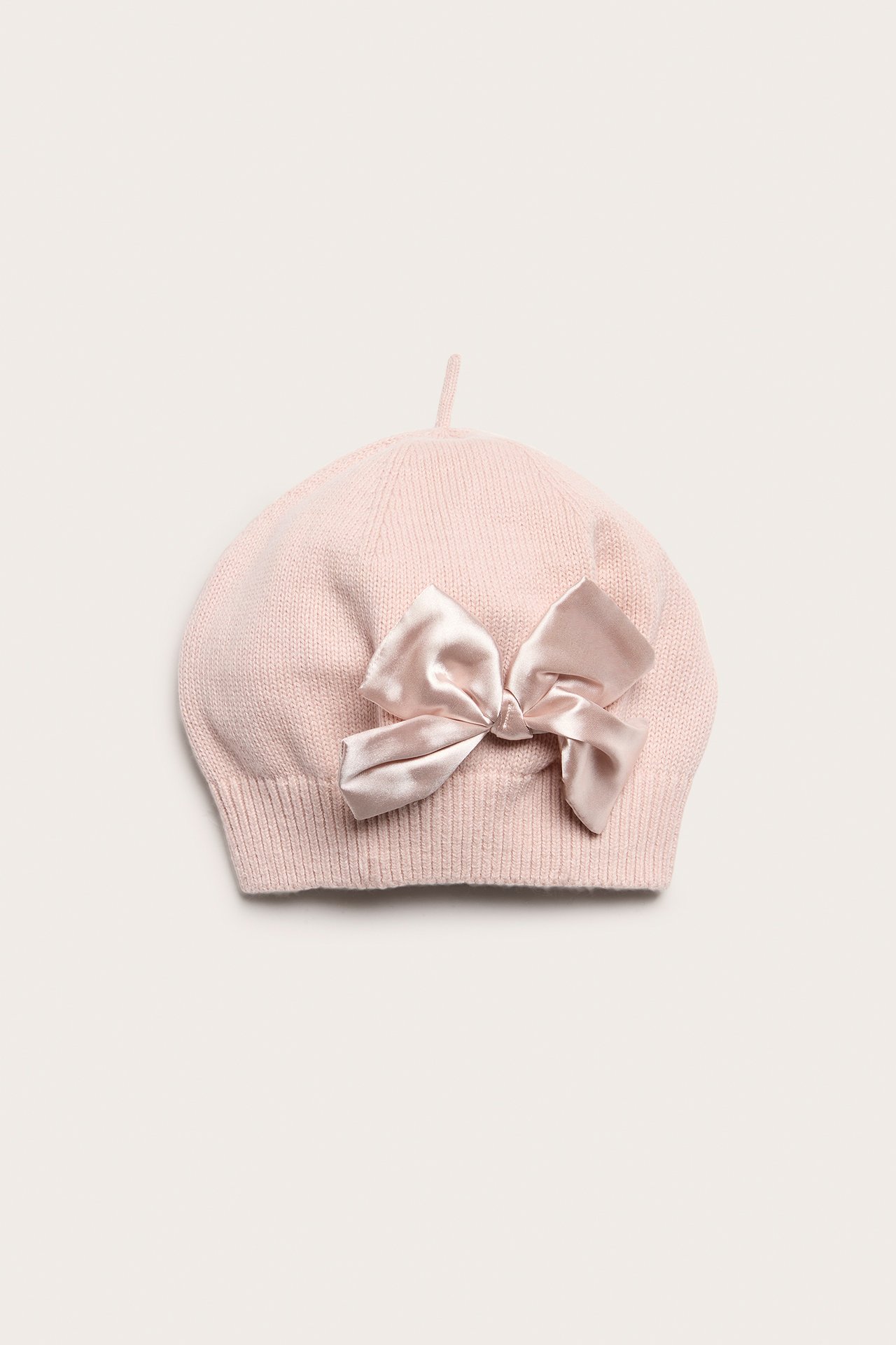 Frontvisning av en lys rosa strikket basker med en skinnende, vevd lys rosa sløyfe.