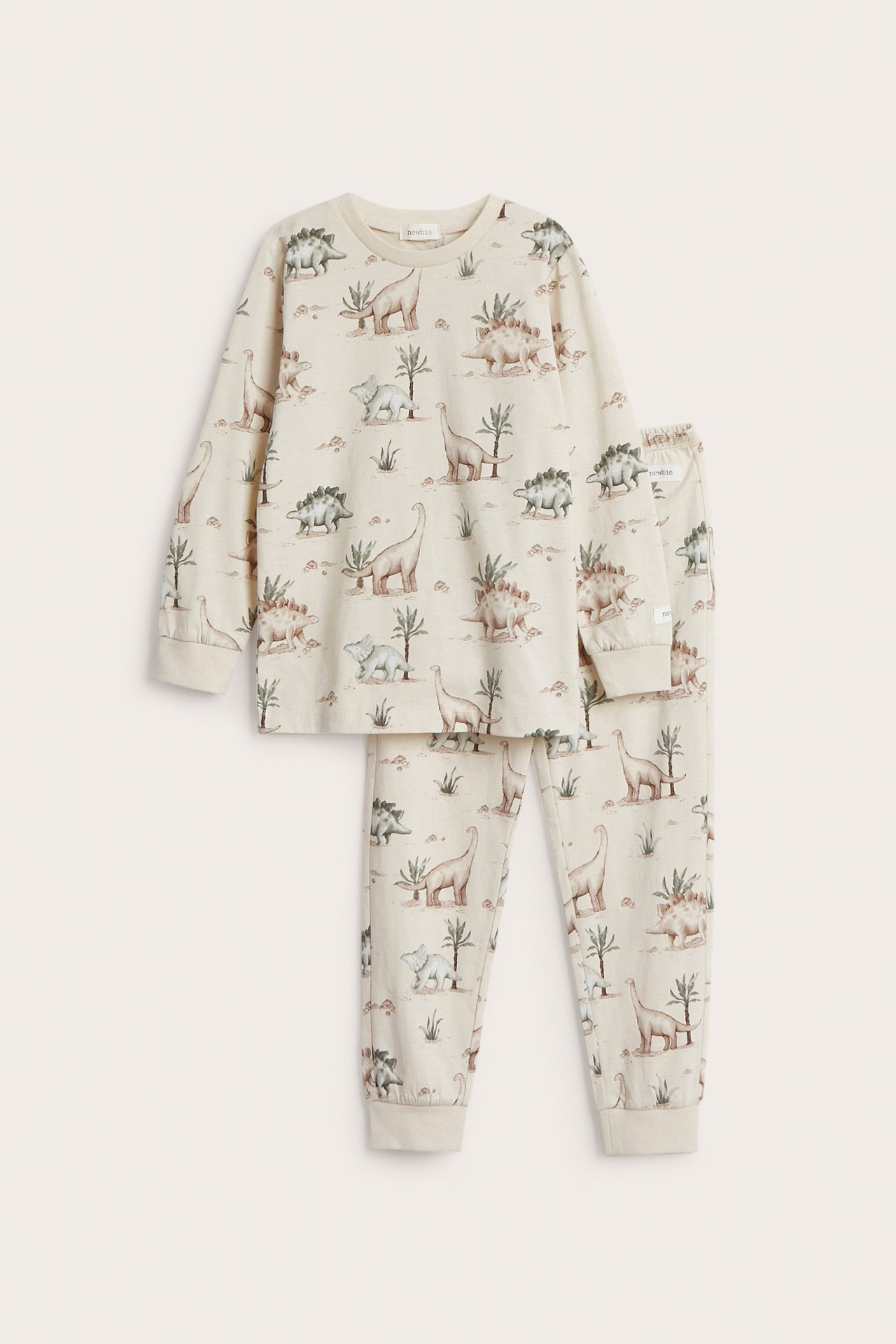 Framifrån: Ljusbeige tvådelad barnpyjamas i trikå med heltäckande dinosauriemönster.