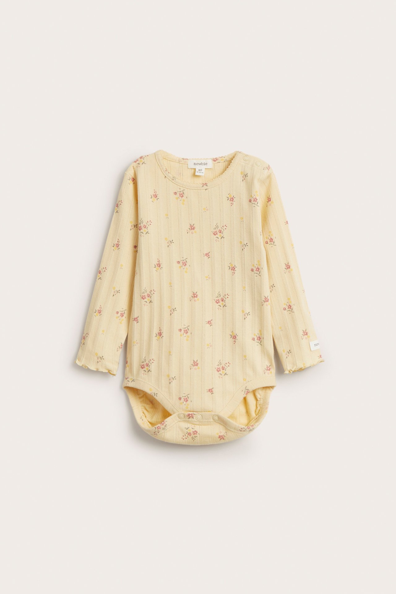 Frontvisning av en gul pointelle ribb babybody med lange ermer, lite blomstertrykk og trykknapper.