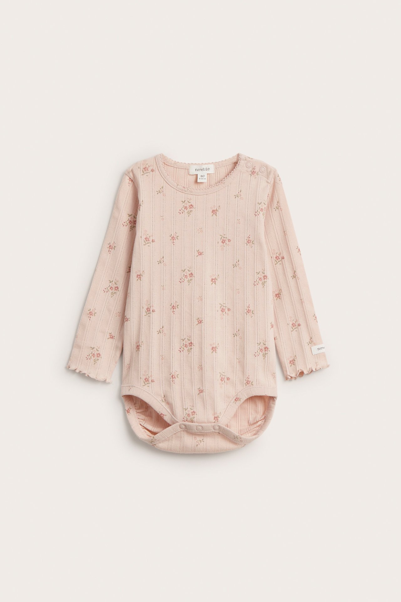 Forfra: lyserosa baby langermet pointelle ribbet body med blomstermønster, bølgete kanter, trykknapper.