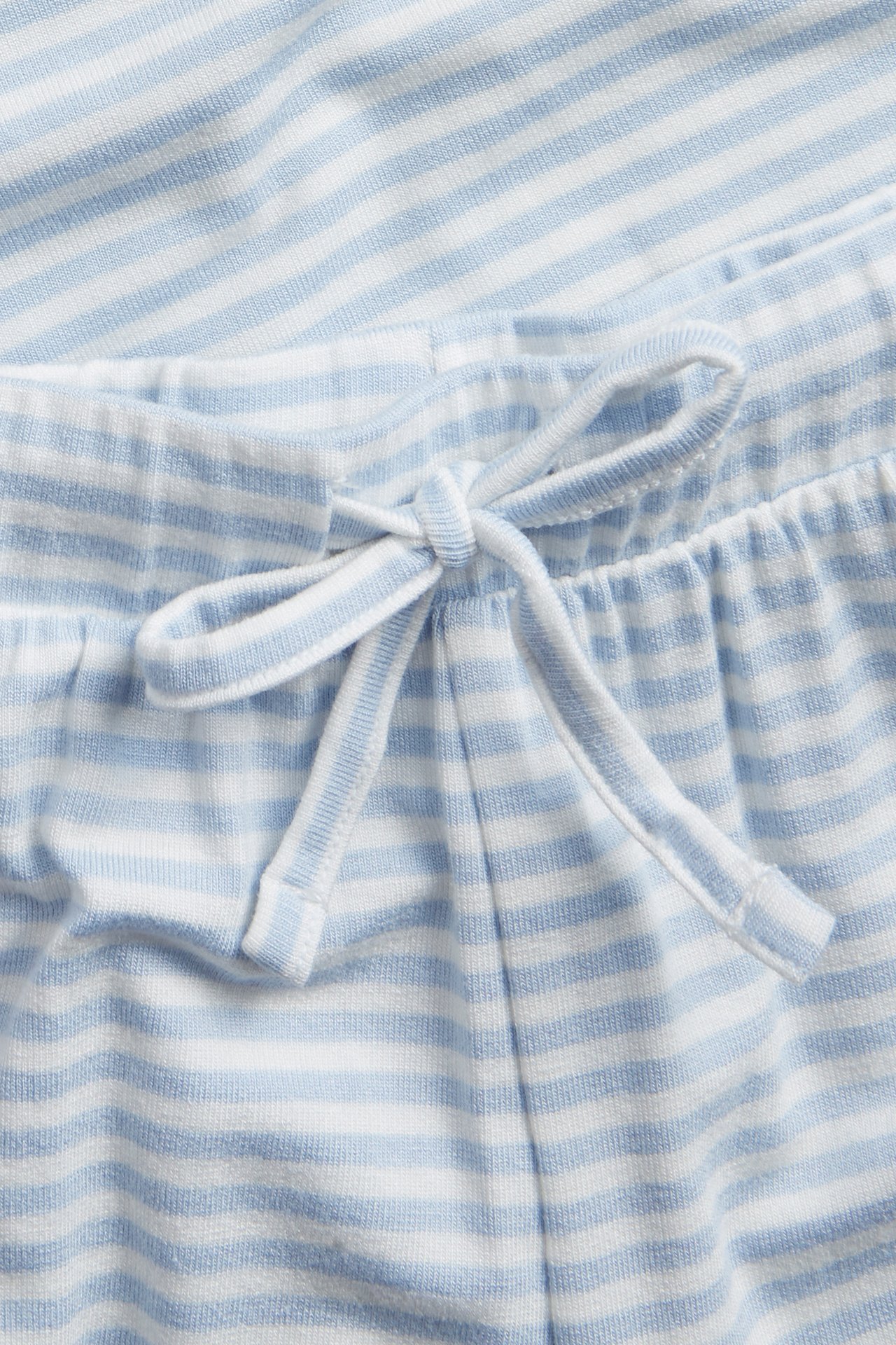 Zbliżenie na jasnoniebieskie i białe, pasiasty dżersejowe spodnie piżamowe ze sznurkiem w pasie.