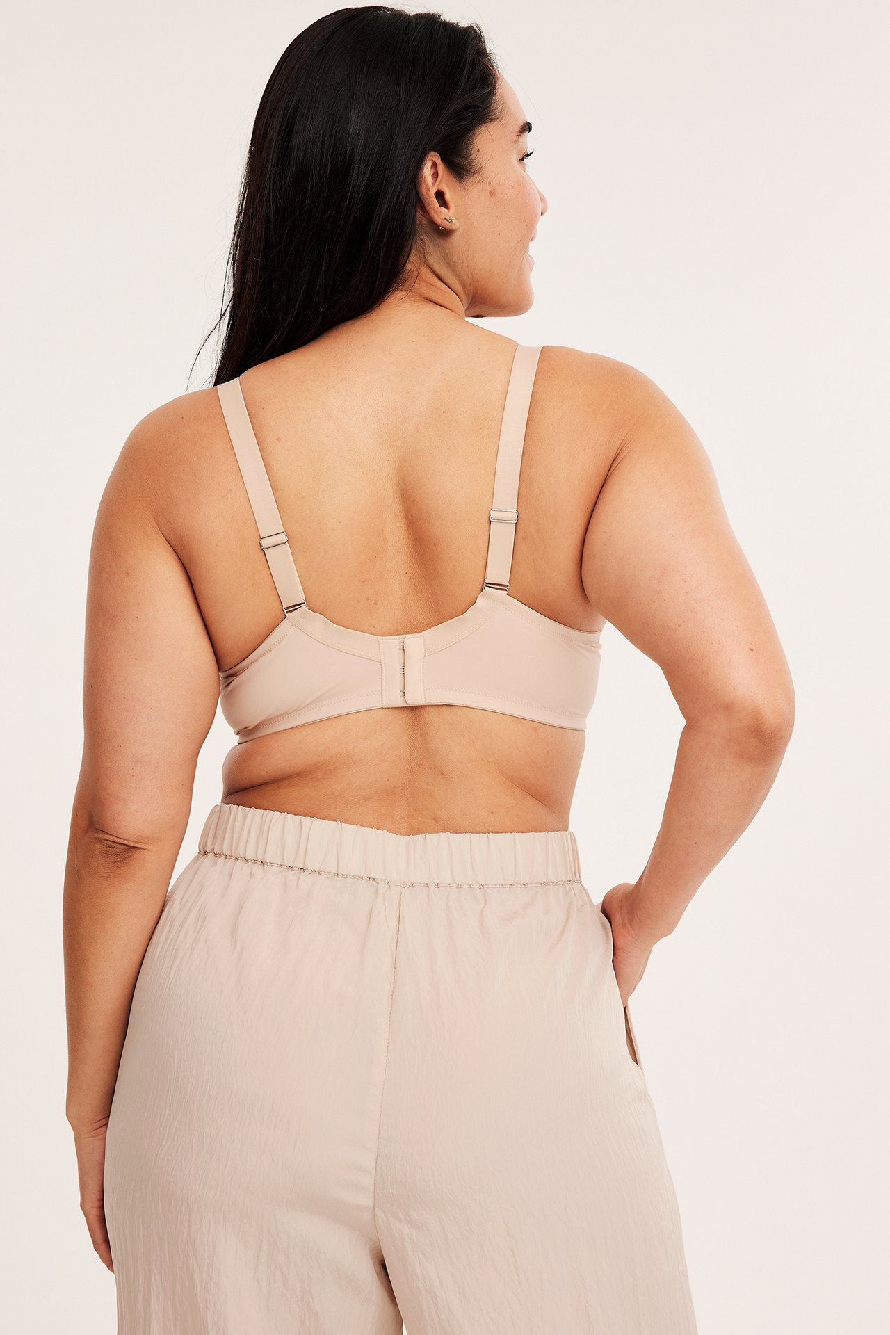 Ryggvisning av kvinne i lys beige push-up BH med brede stropper og lys beige elastiske bukser.