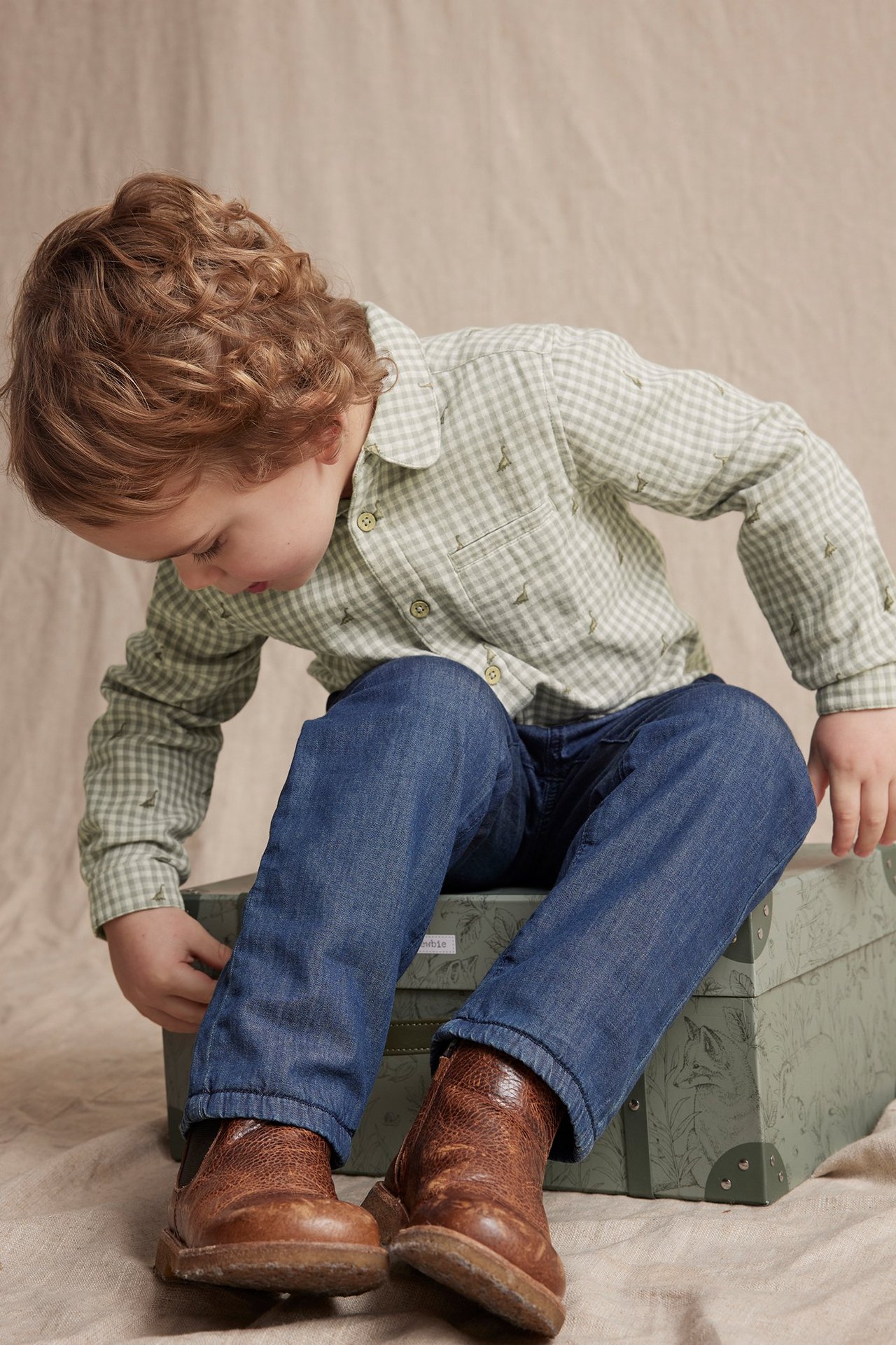 Barn i lysegrønn- og hvitrutet bomullsskjorte med broderi, lomme, blå jeans og brune støvler.