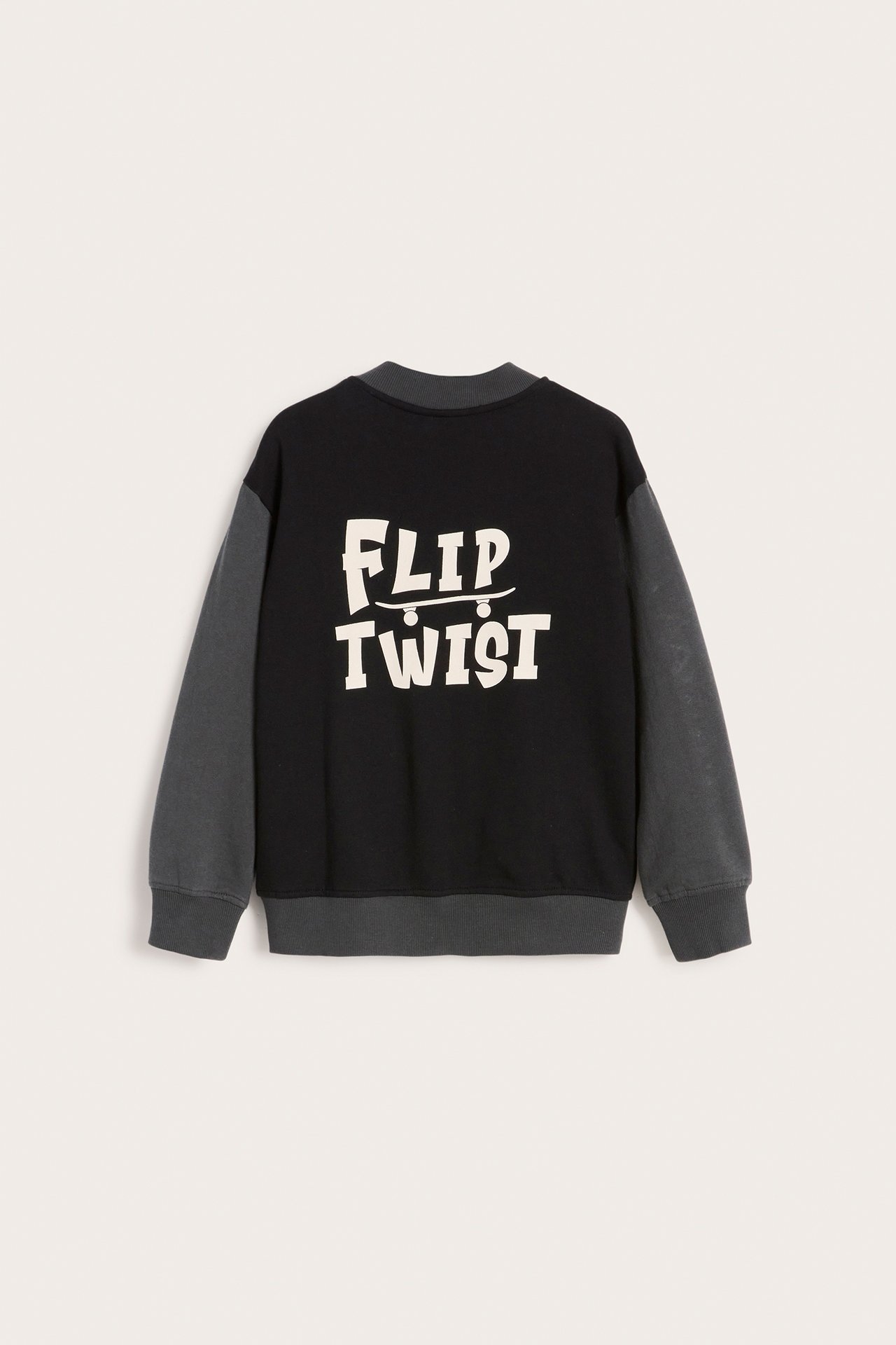 Bakfra av en svart og mørkegrå baseballjakke for barn med hvitt 'FLIP TWIST' skateboardtrykk.