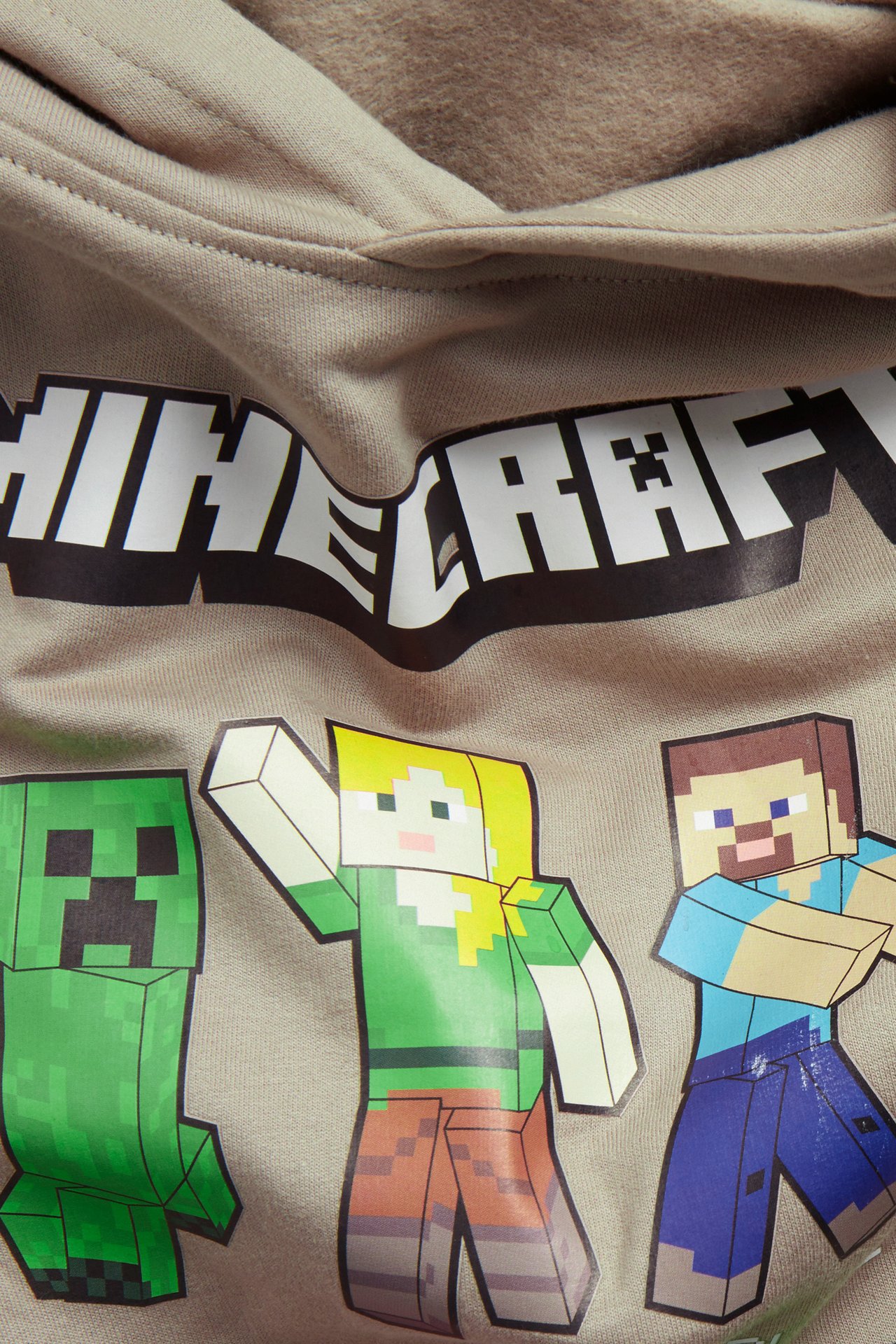 Zbliżenie beżowej bawełnianej bluzy z kapturem z dużym logo Minecraft i nadrukiem postaci z przodu.