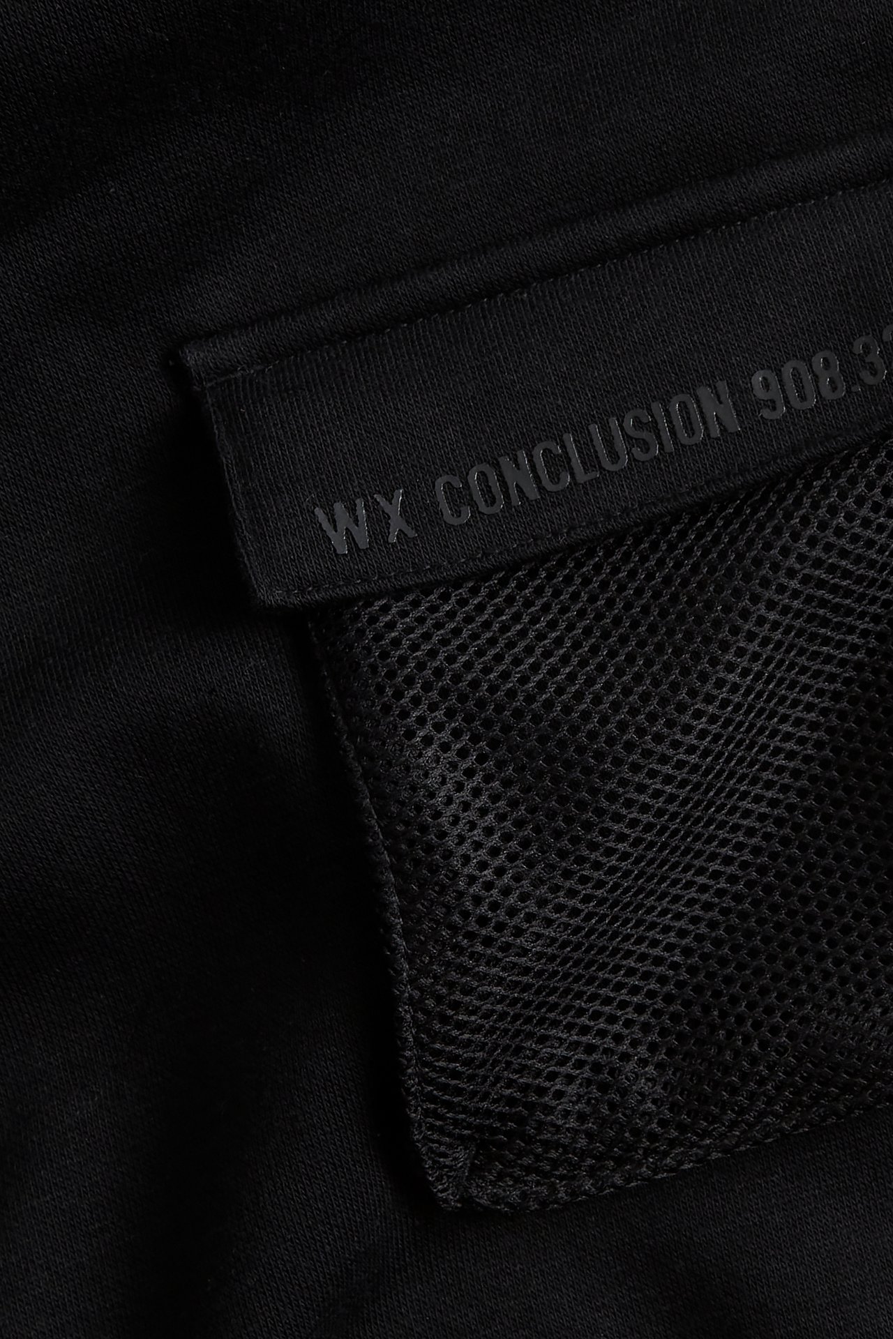 Lähikuva mustasta hupparista, jossa on verkkorintatasku ja musta läppä 'WX CONCLUSION' -painatuksella.