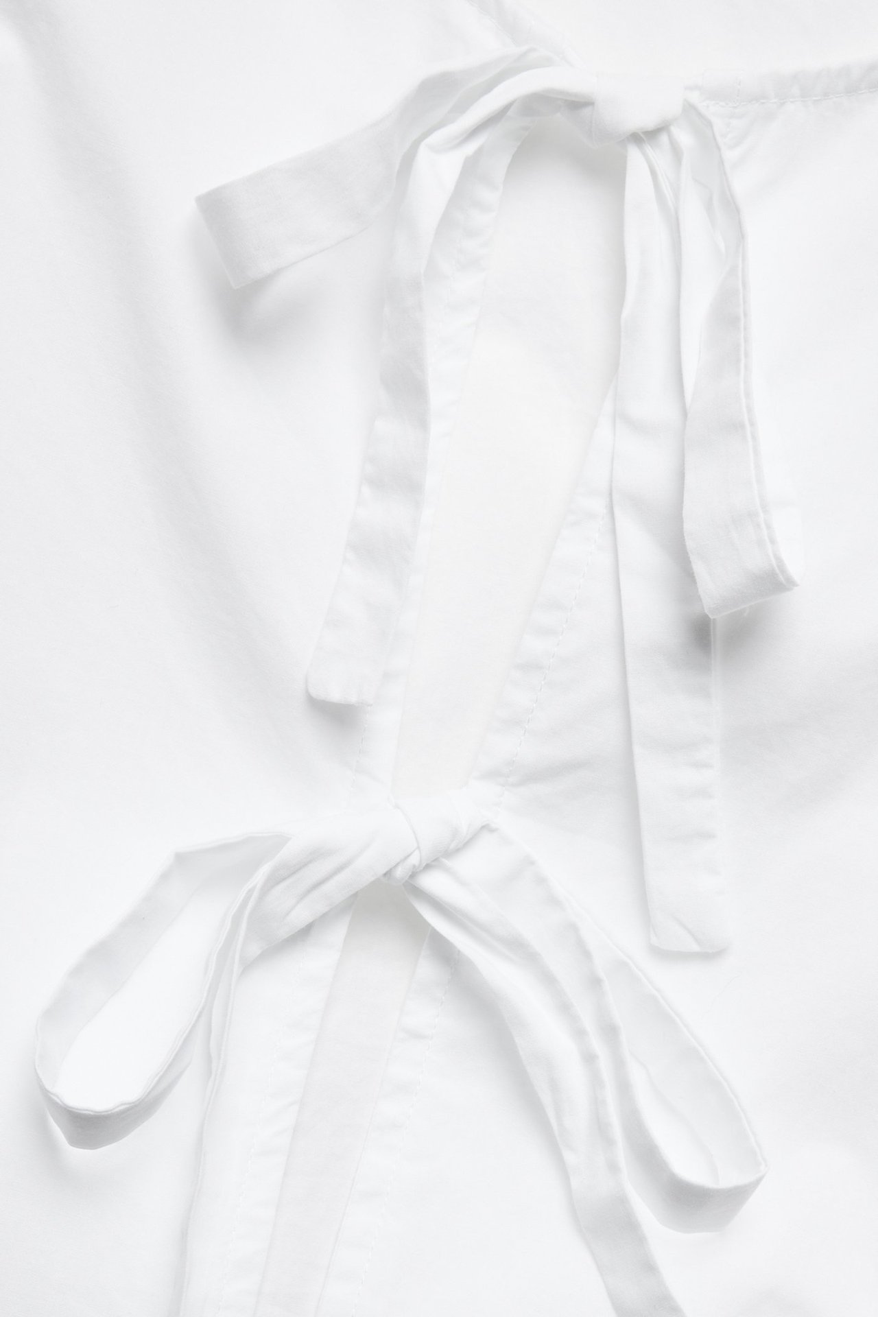 Zbliżenie białej bawełnianej bluzki z dwoma wiązaniami z przodu.