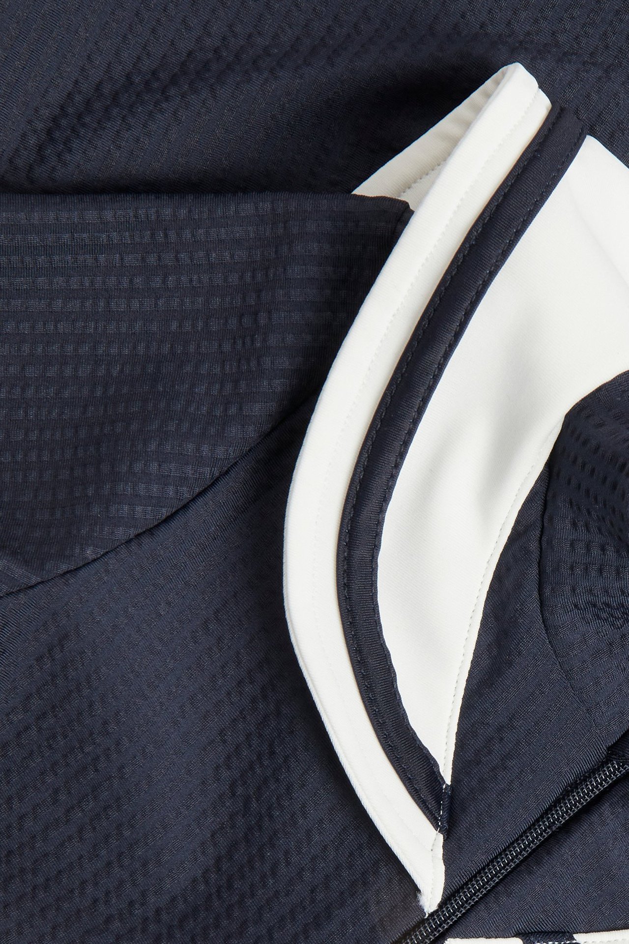 Närbild av en mörkblå UV-dräkt i strukturjersey med vit sjömanskrage och dragkedja fram.