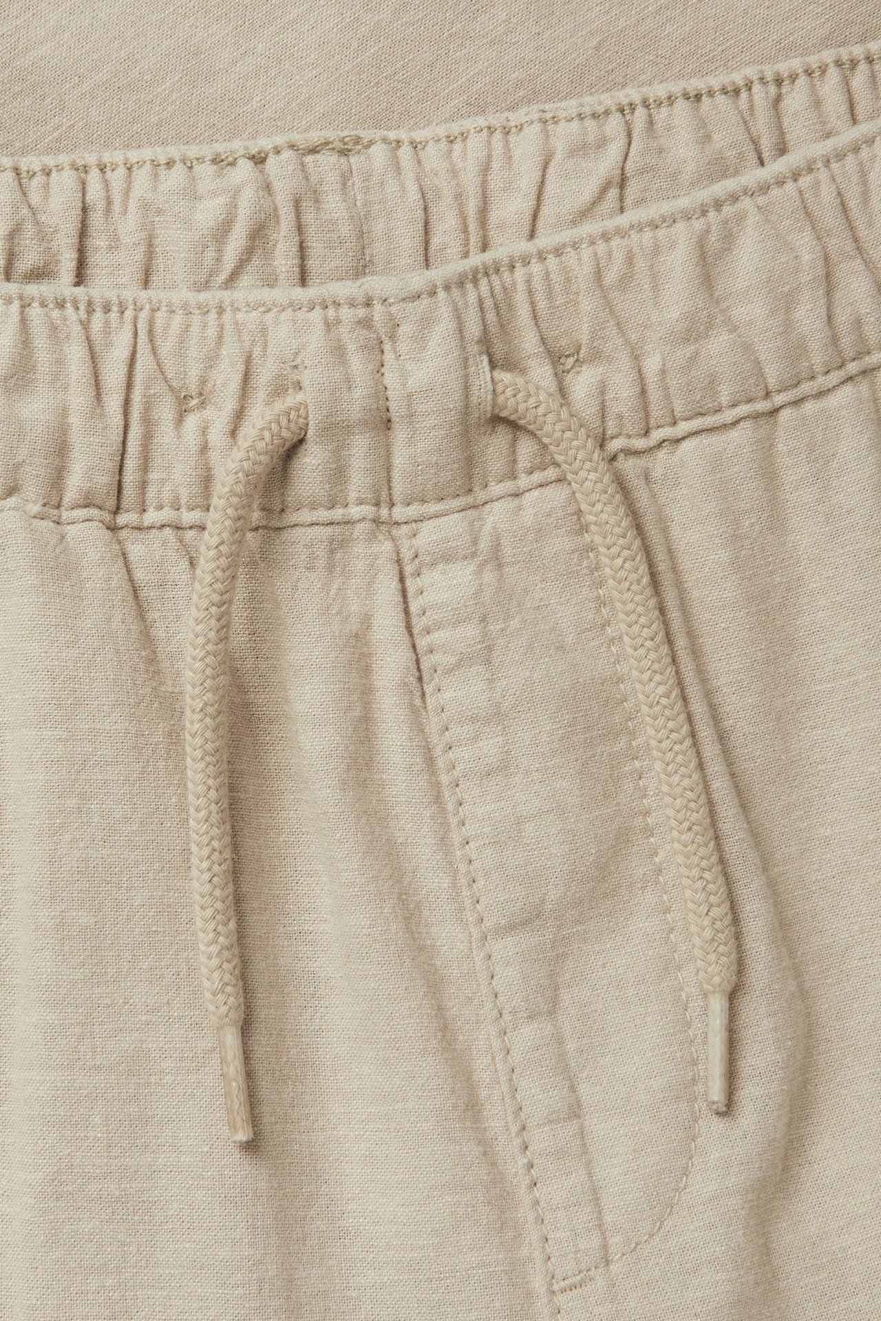 Zbliżenie beżowych spodni z mieszanki lnu z elastycznym pasem ze sznurkiem.