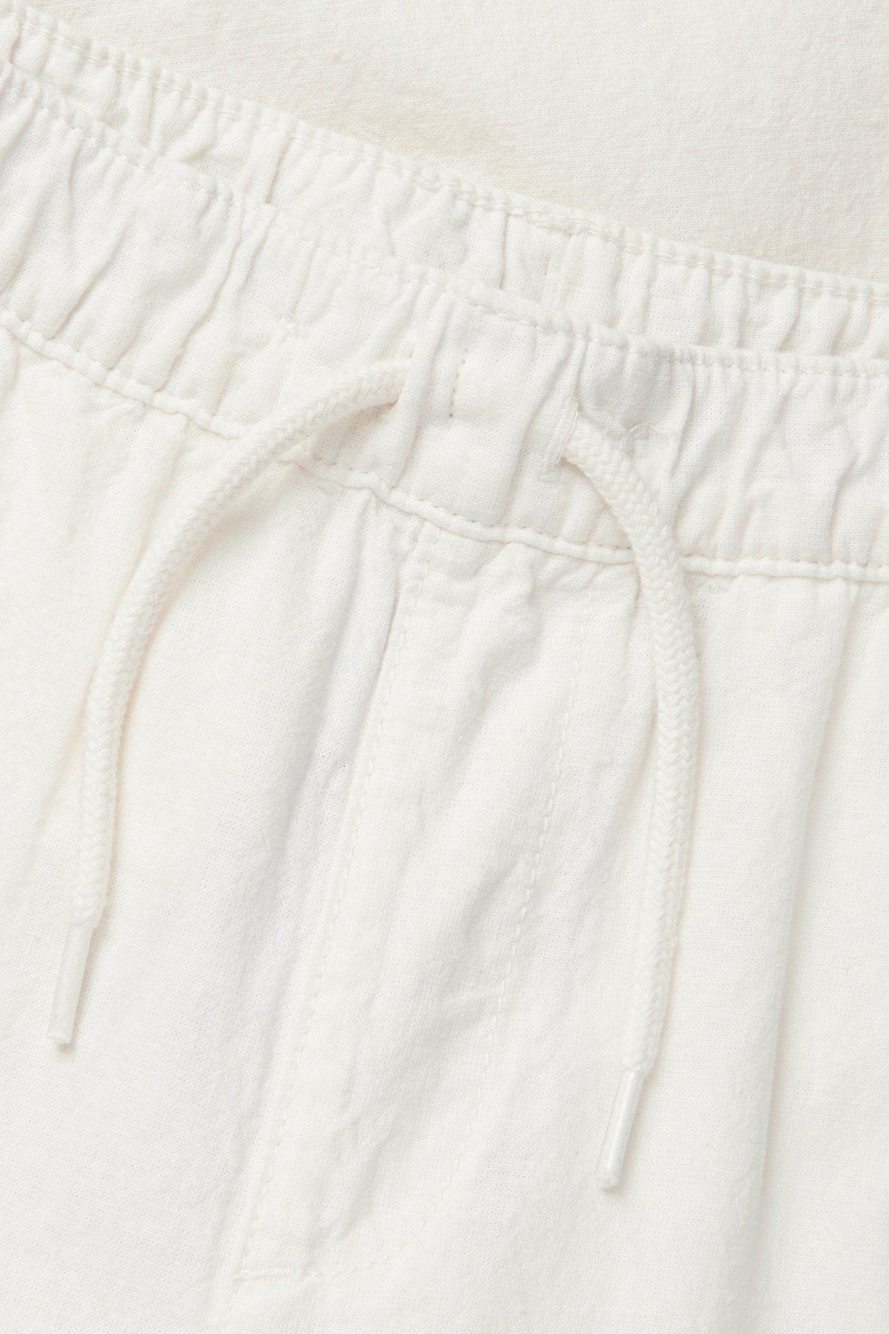 Zbliżenie na ecru spodnie z mieszanki lnu z elastyczną talią i sznurkiem.