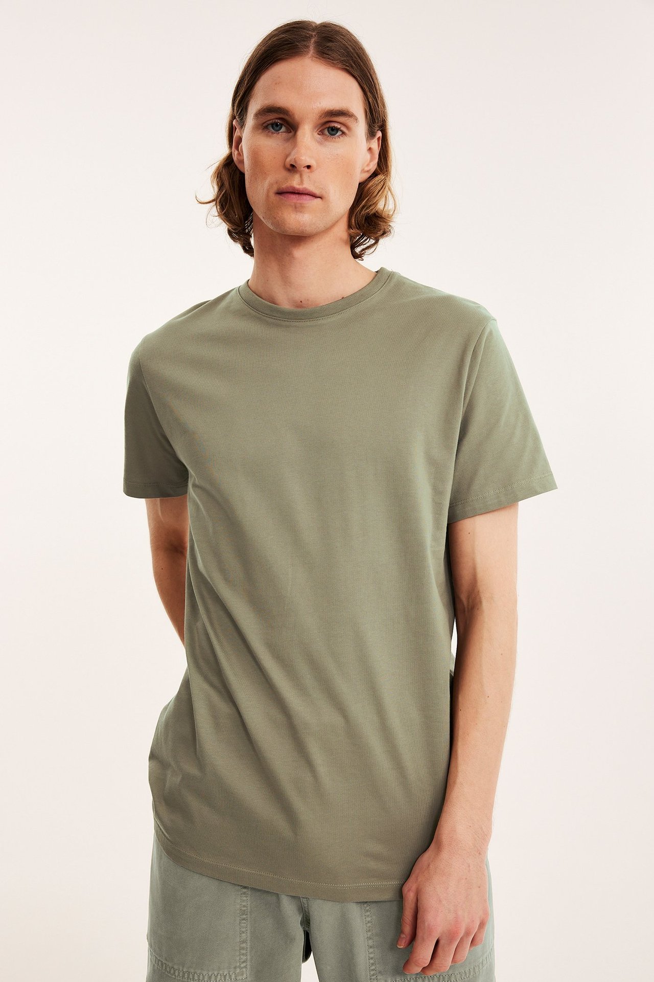 Edestäpäin, mies yllään yksivärinen khakinvihreä pyöreäkauluksinen puuvilla-T-paita ja yhteensopivat shortsit.