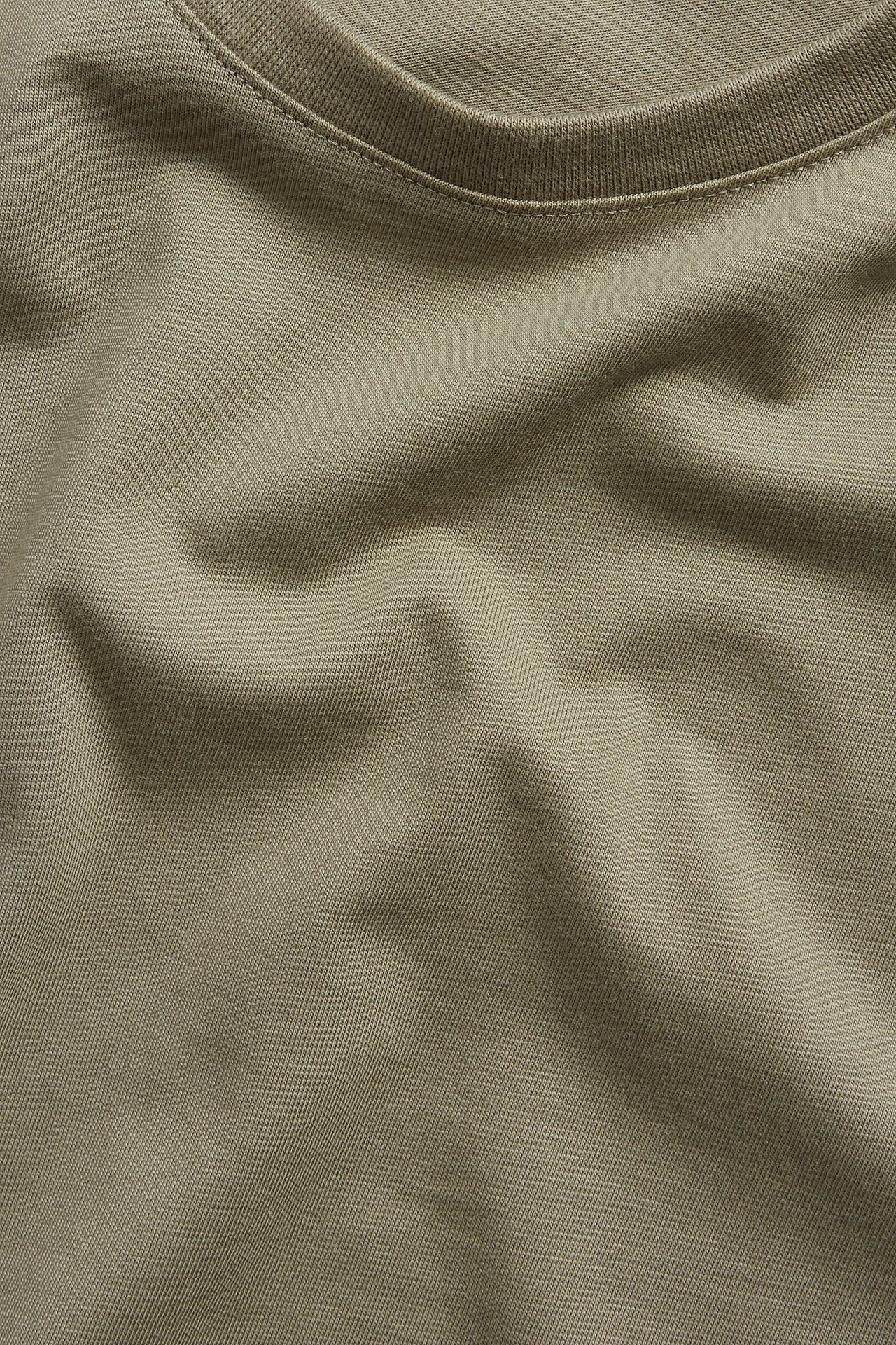 Zbliżenie męskiego jednolitego t-shirtu z okrągłym dekoltem w kolorze khaki, z bawełny, pokazuje tkaninę i dekolt.