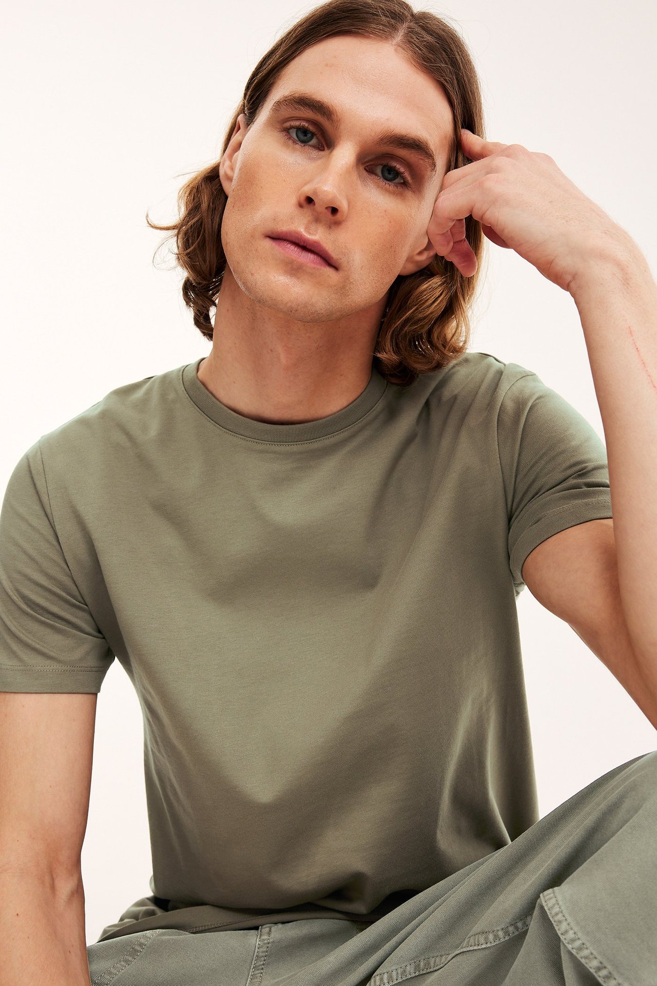 Widok z przodu mężczyzny w khaki zielonym T-shircie z okrągłym dekoltem i pasujących spodniach.