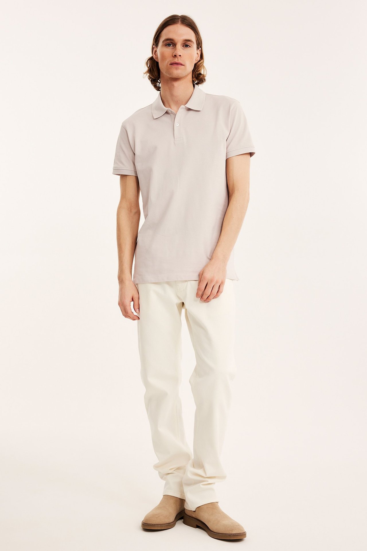 Koko etunäkymä miehestä yllään vaaleanbeige puuvillapikeepaita, luonnonvalkoiset housut ja vaaleanruskeat mokkanilkkurit.