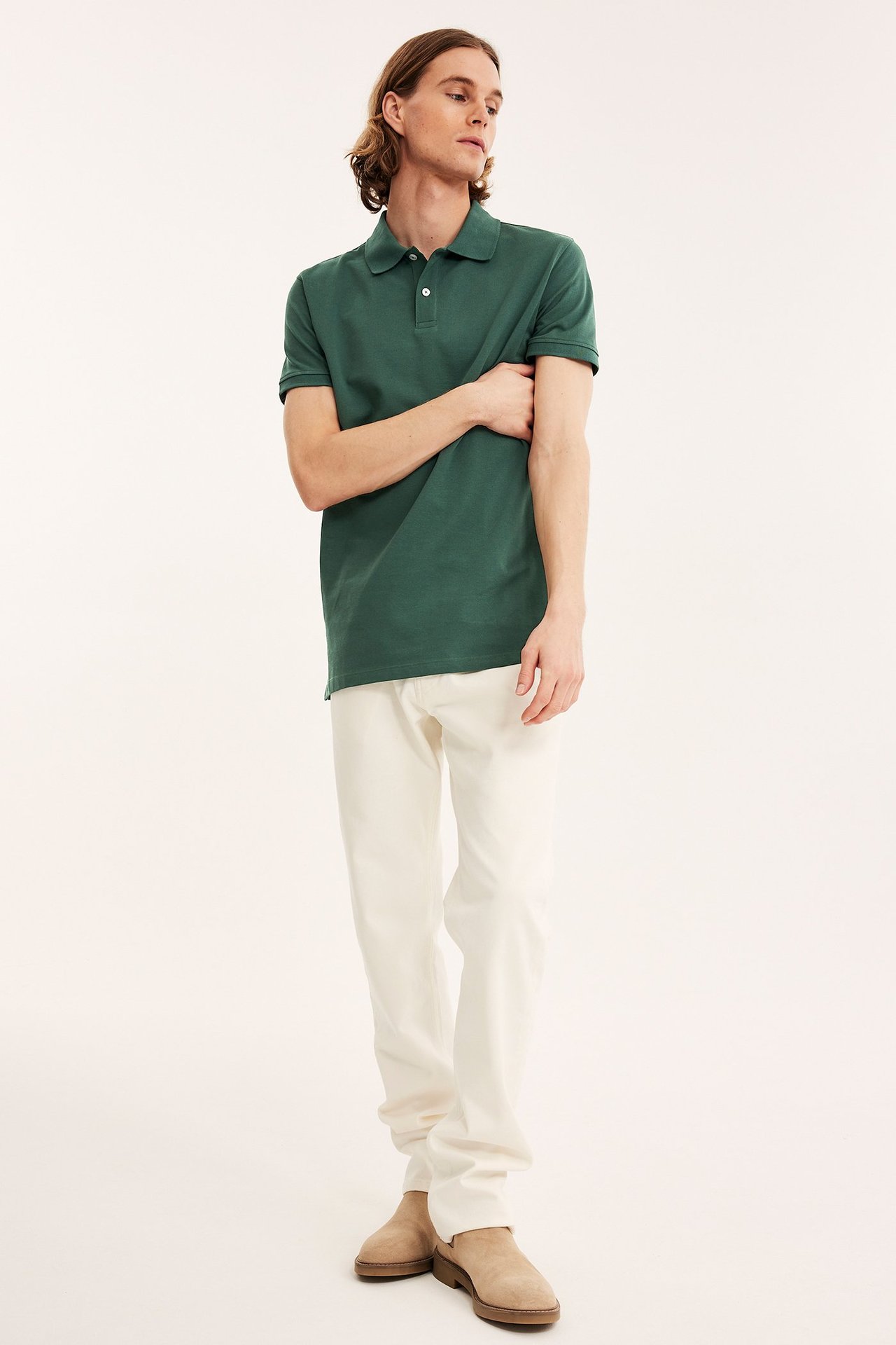 Edestä: mies tummanvihreässä puuvillapoolopaidassa 2 napilla, kermanvärisissä housuissa, beigessä mokkanahkakengissä.