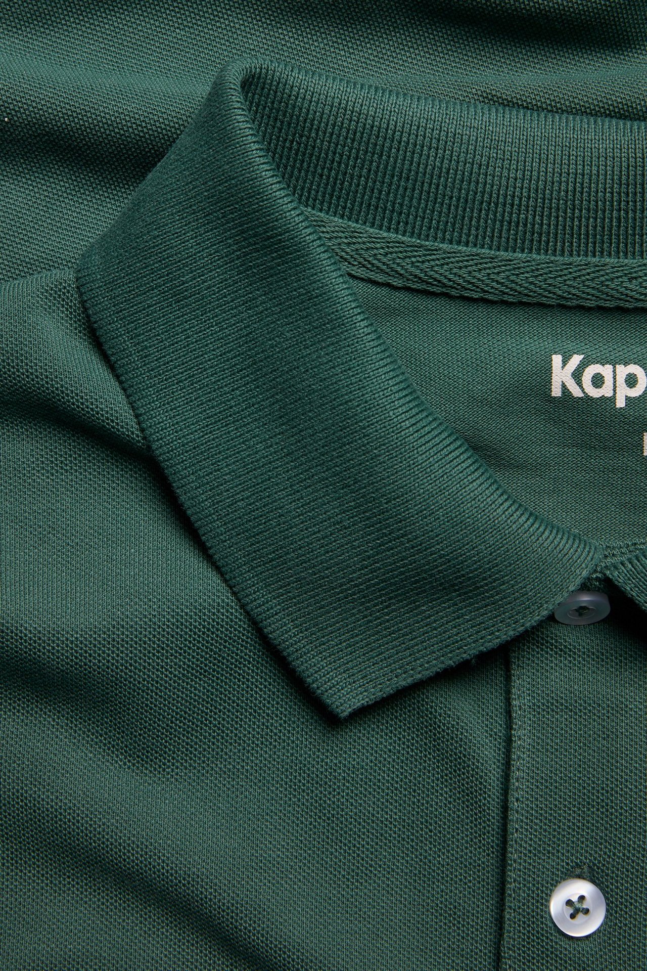 Zbliżenie na męską jednolitą zieloną bawełnianą koszulkę polo z kołnierzykiem i białymi guzikami.