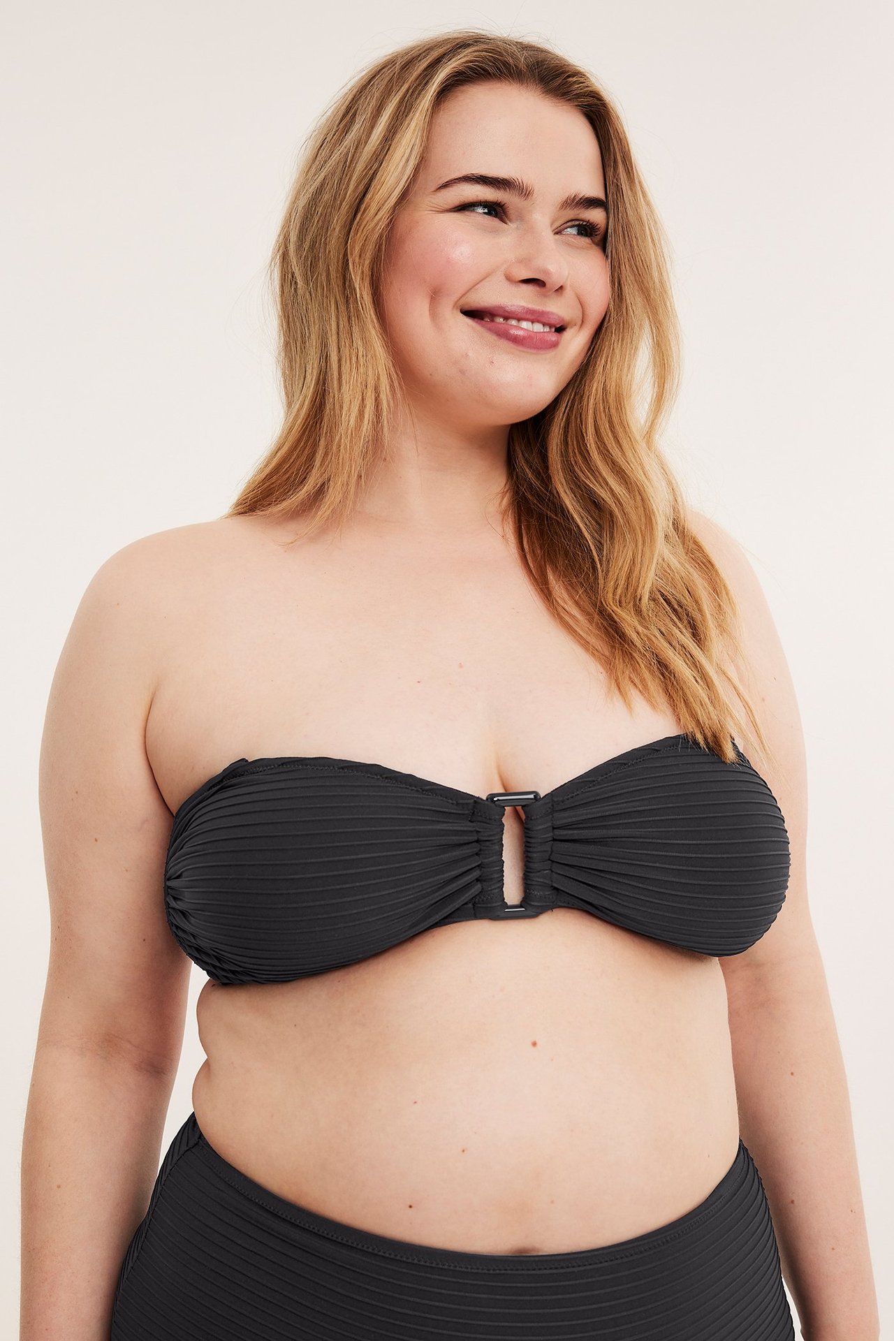 Framifrån, kvinna i svart strukturerad bandeau-bikinitopp med spänne fram och matchande underdel.