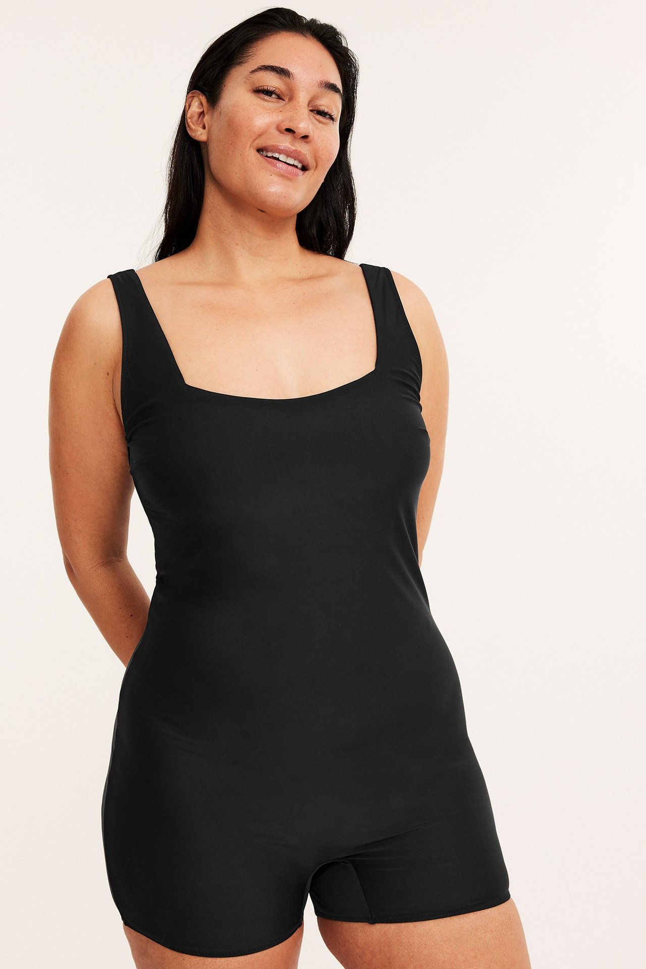 Widok z przodu uśmiechniętej kobiety w czarnym jednolitym stroju kąpielowym z krótkimi nogawkami.