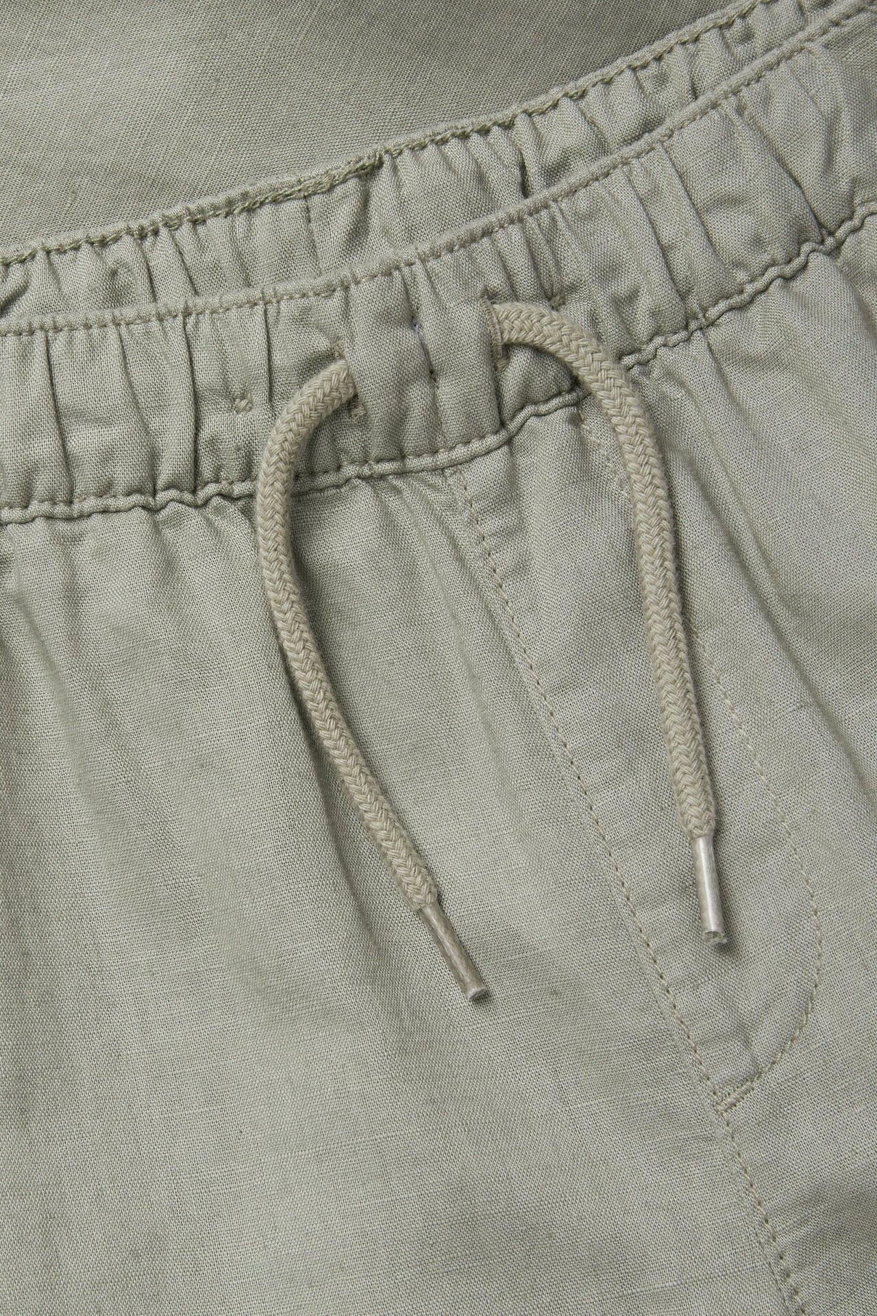 Zbliżenie zielonych spodni z mieszanki lnu z elastycznym pasem i jasnobeżowym sznurkiem.