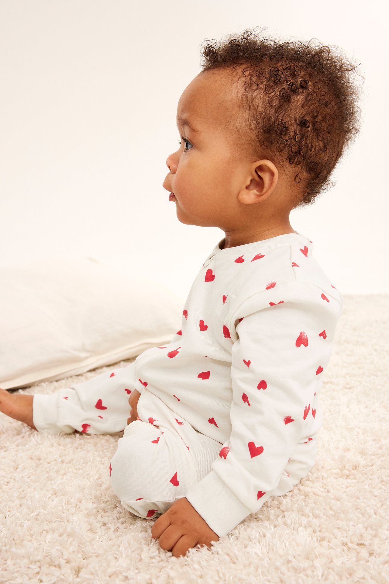 Sidebilde av en baby i en offwhite langermet pysjamas med rødt hjerteprint.