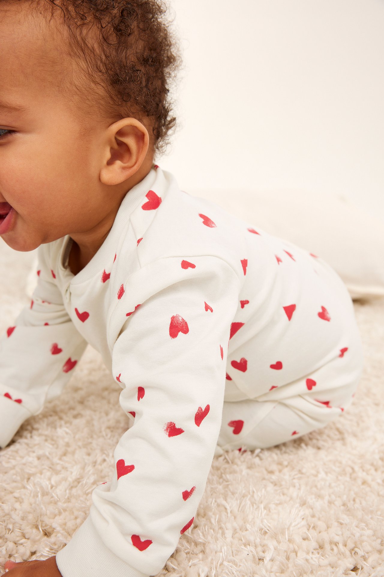 Sidebilde av en baby i en offwhite bomullsromper med rødt hjertemønster.