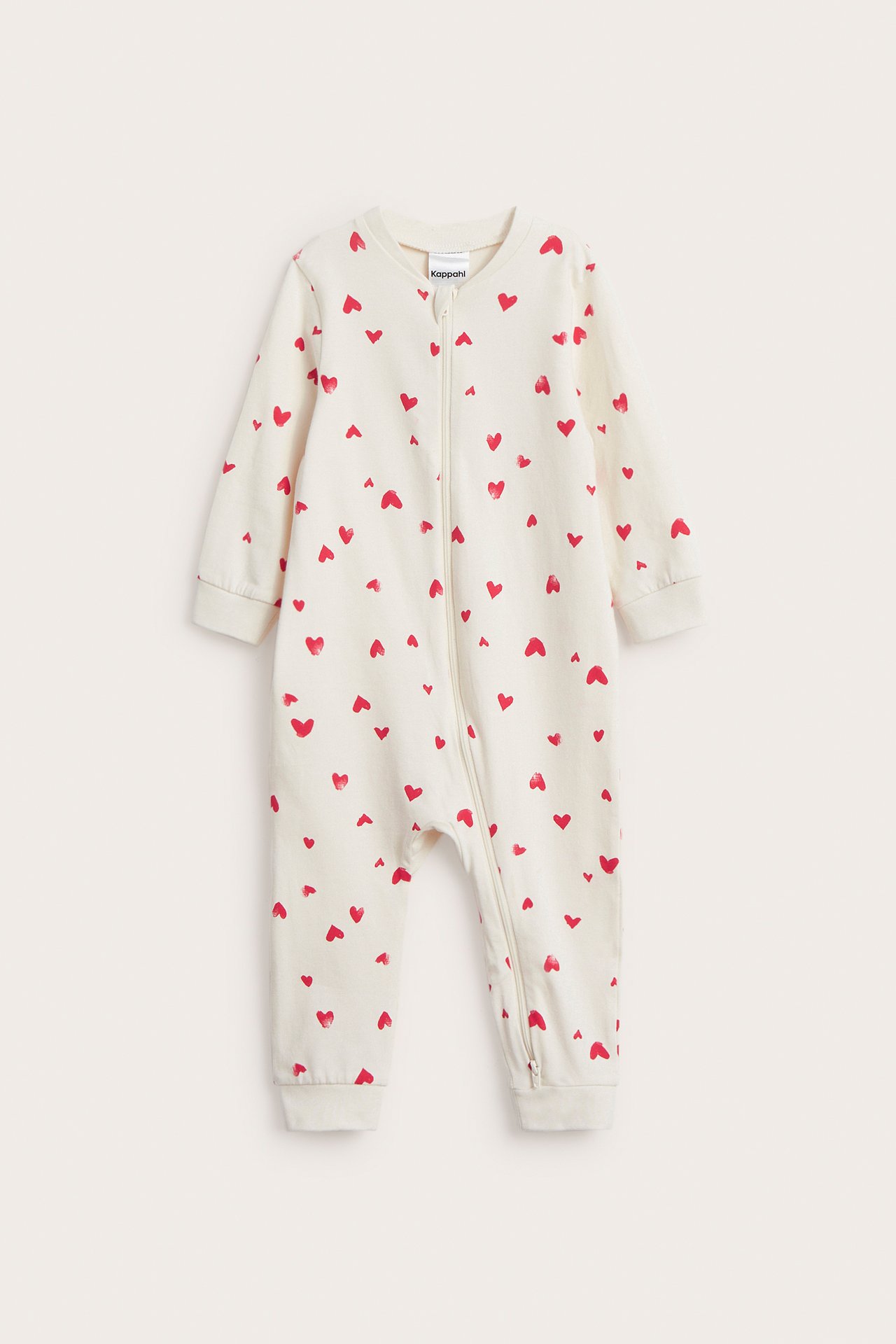 Frontvisning av en off-white baby-pysjamas med rødt hjertemønster og hellang glidelås.